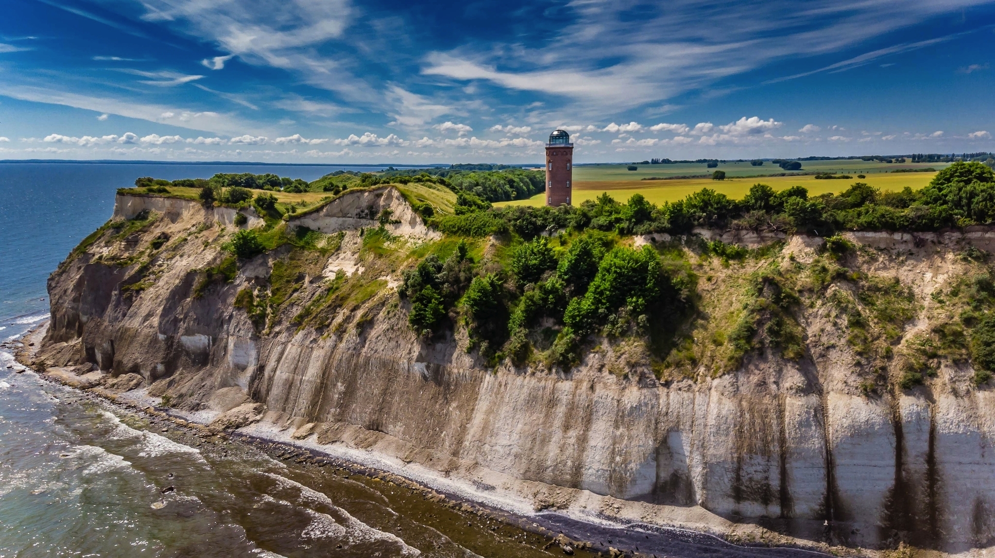 Klippenlandschaft mit Leuchtturm und bewölktem Himmel am Meer.