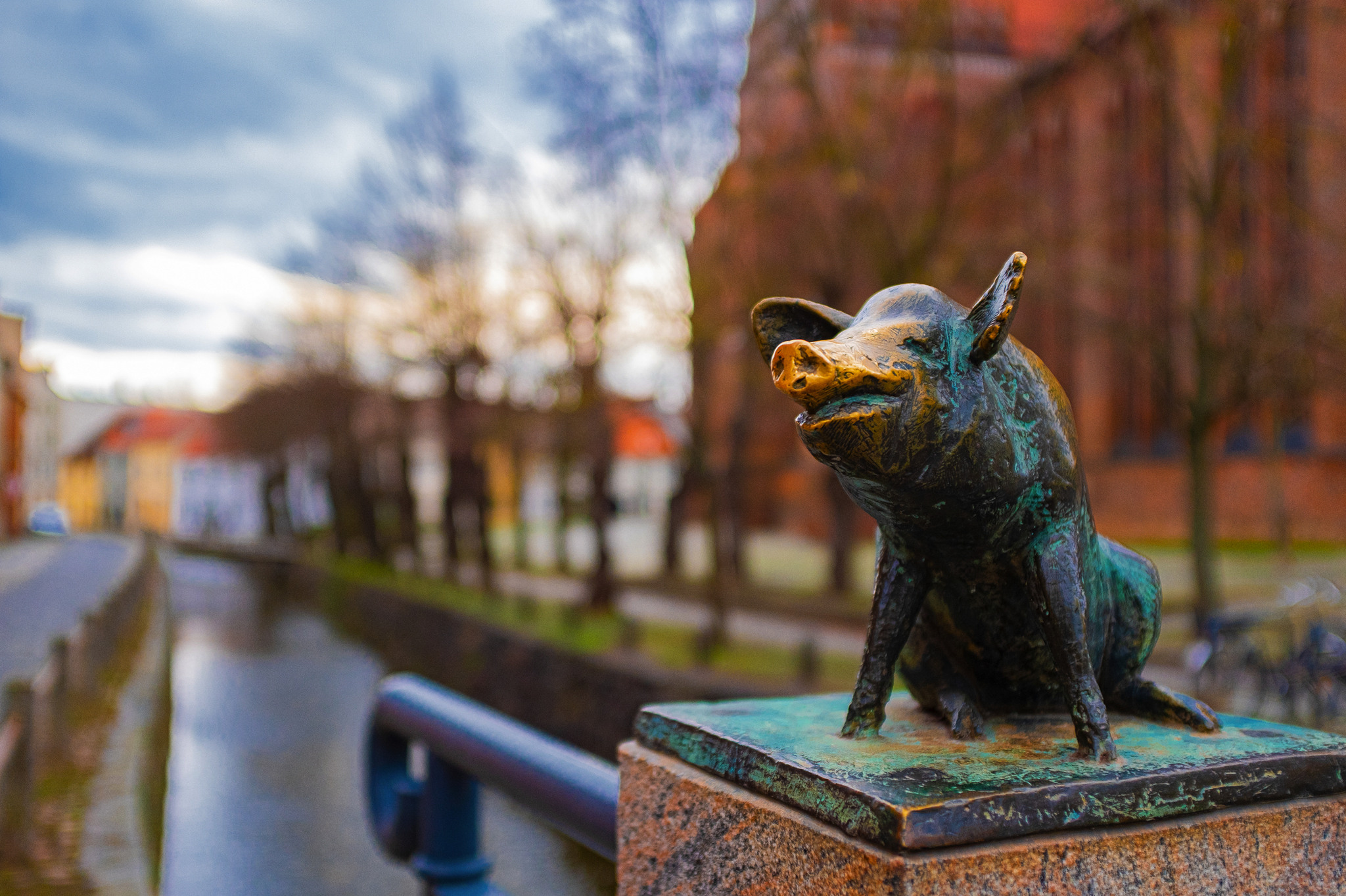 Das Bild zeigt eine Statue eines Glücksschweins auf der Schweinsbrücke in Wismar, Mecklenburg-Vorpommern, Deutschland, an der Ostseeküste im Winter. Im Hintergrund sind ein Kanal und eine Kirche zu sehen.