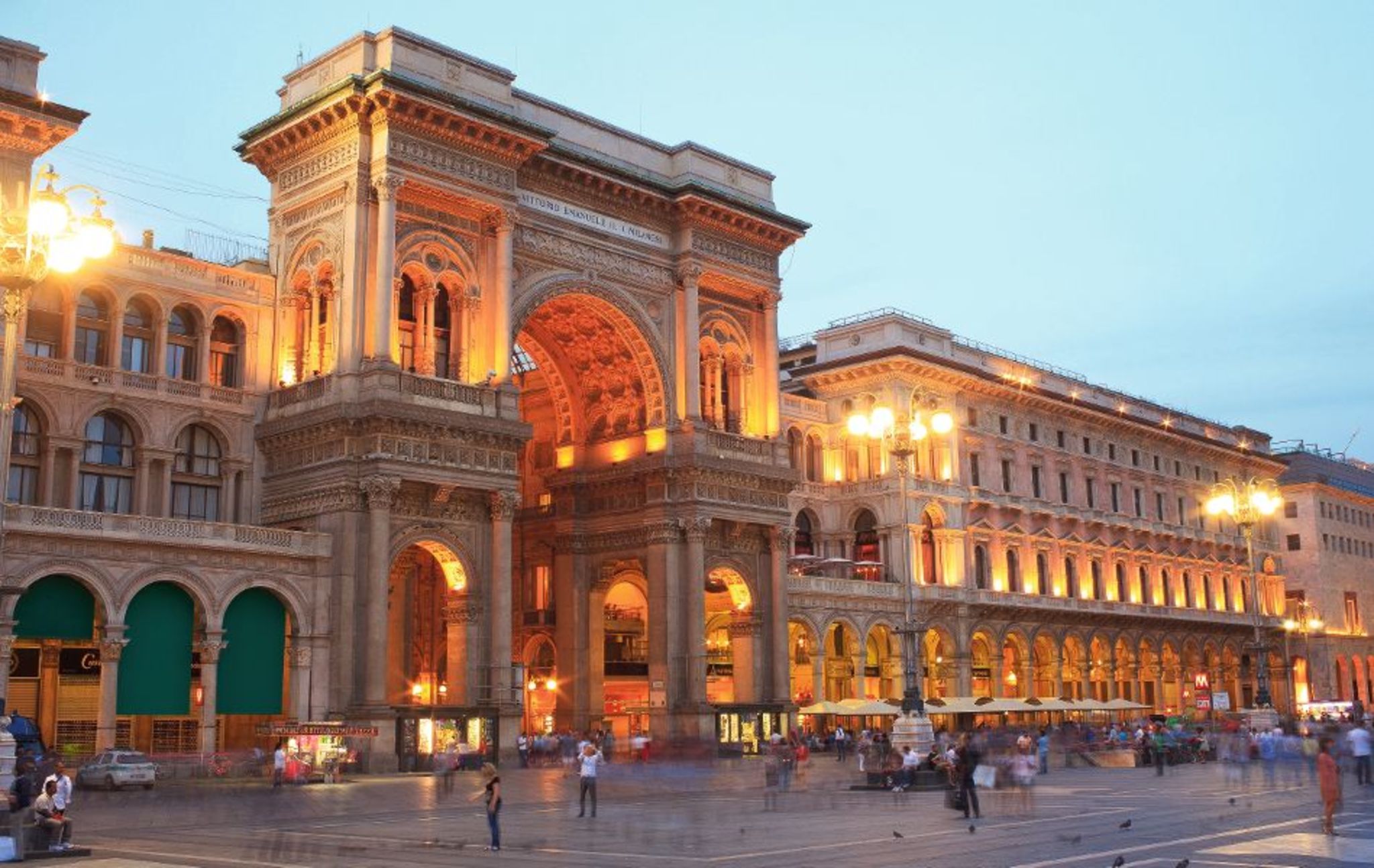 Historisches Gebäude am Abend mit beleuchteten Bögen und belebtem Platz.