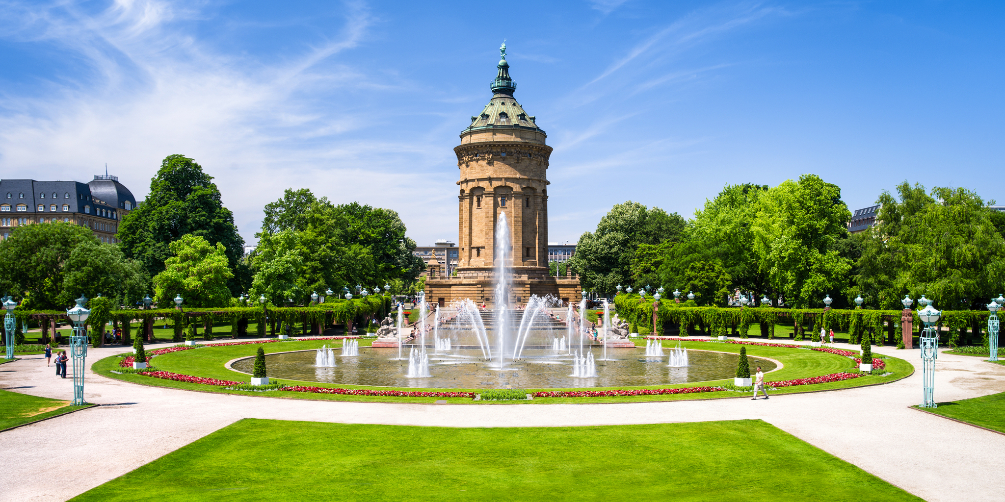 Wasserturm in einem Park mit Brunnen und grüner Umgebung bei klarem Himmel.