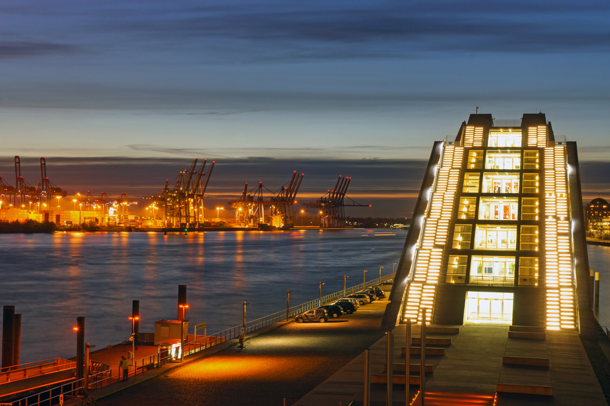 Hafen in Hamburg nach Sonnenuntergang mit beleuchteten Gebäuden und Kränen entlang der Elbe.