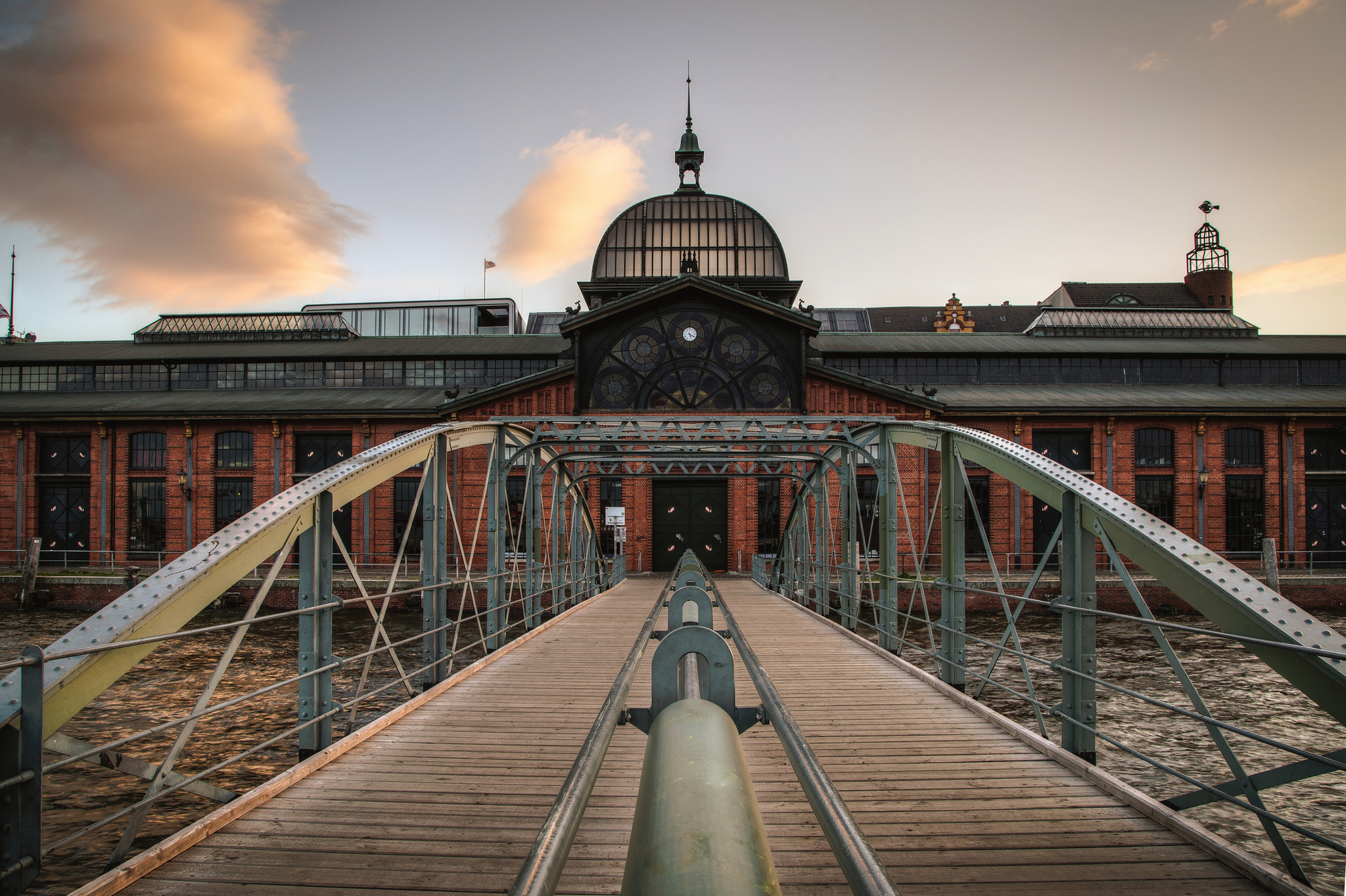 Fischauktionshalle in Hamburg mit Brücke im Vordergrund bei Sonnenuntergang.