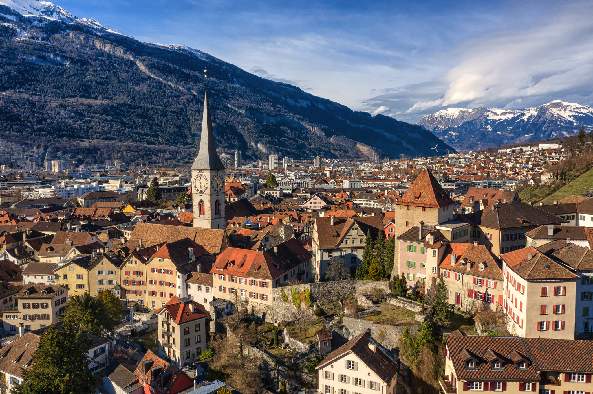 Panorama einer Stadt mit Kirche und Bergen im Hintergrund.