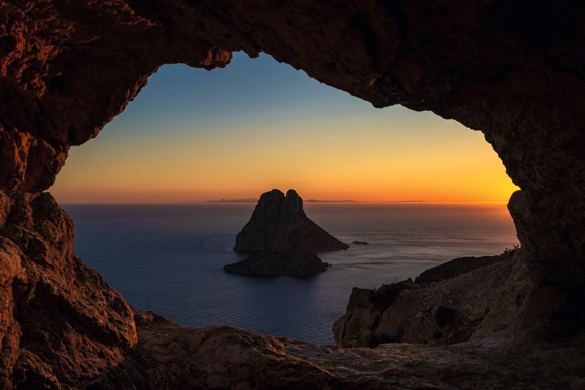 Blick durch eine Felshöhle auf eine Insel bei Sonnenuntergang.