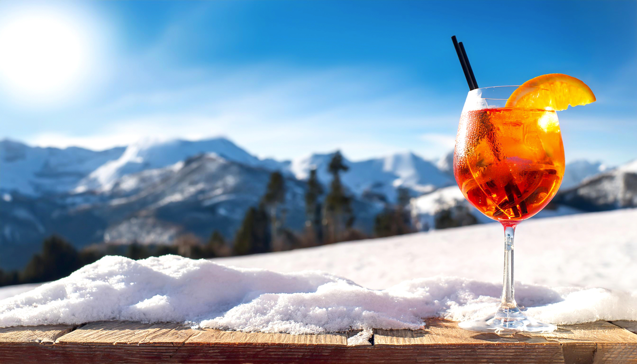 Cocktailglas auf Holztisch im Schnee, Berge im Hintergrund.