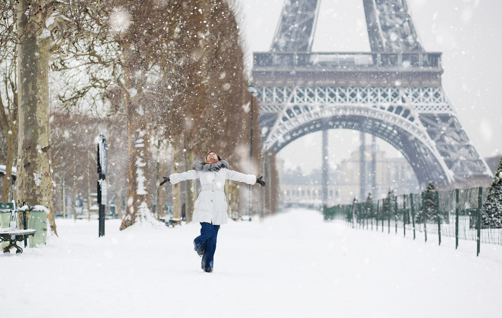 Eine Person steht mit ausgebreiteten Armen im Schnee vor dem Eiffelturm in Paris im Winter.