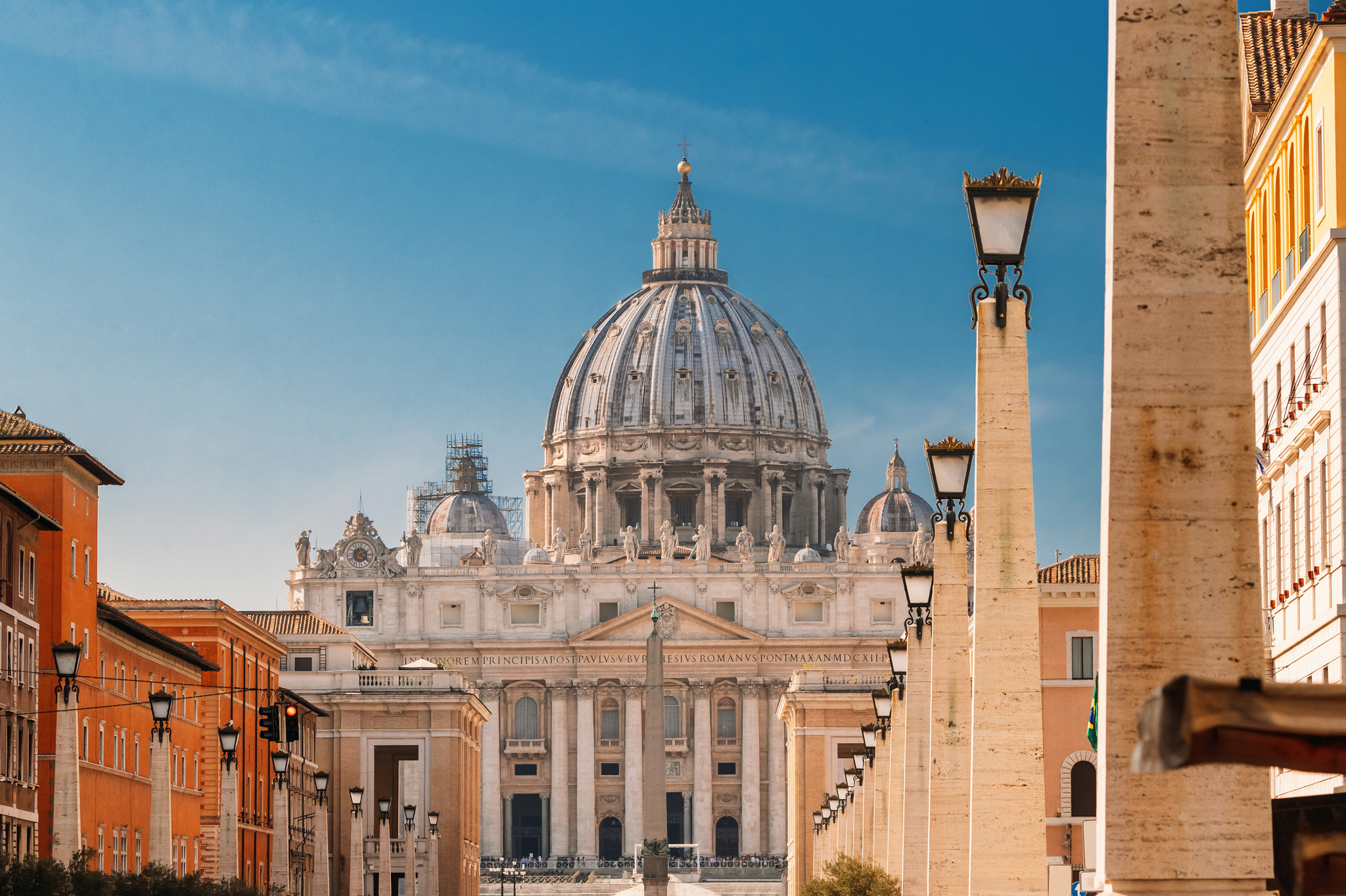 Kuppel des Petersdoms in Rom, umgeben von Säulen und blauen Himmel.