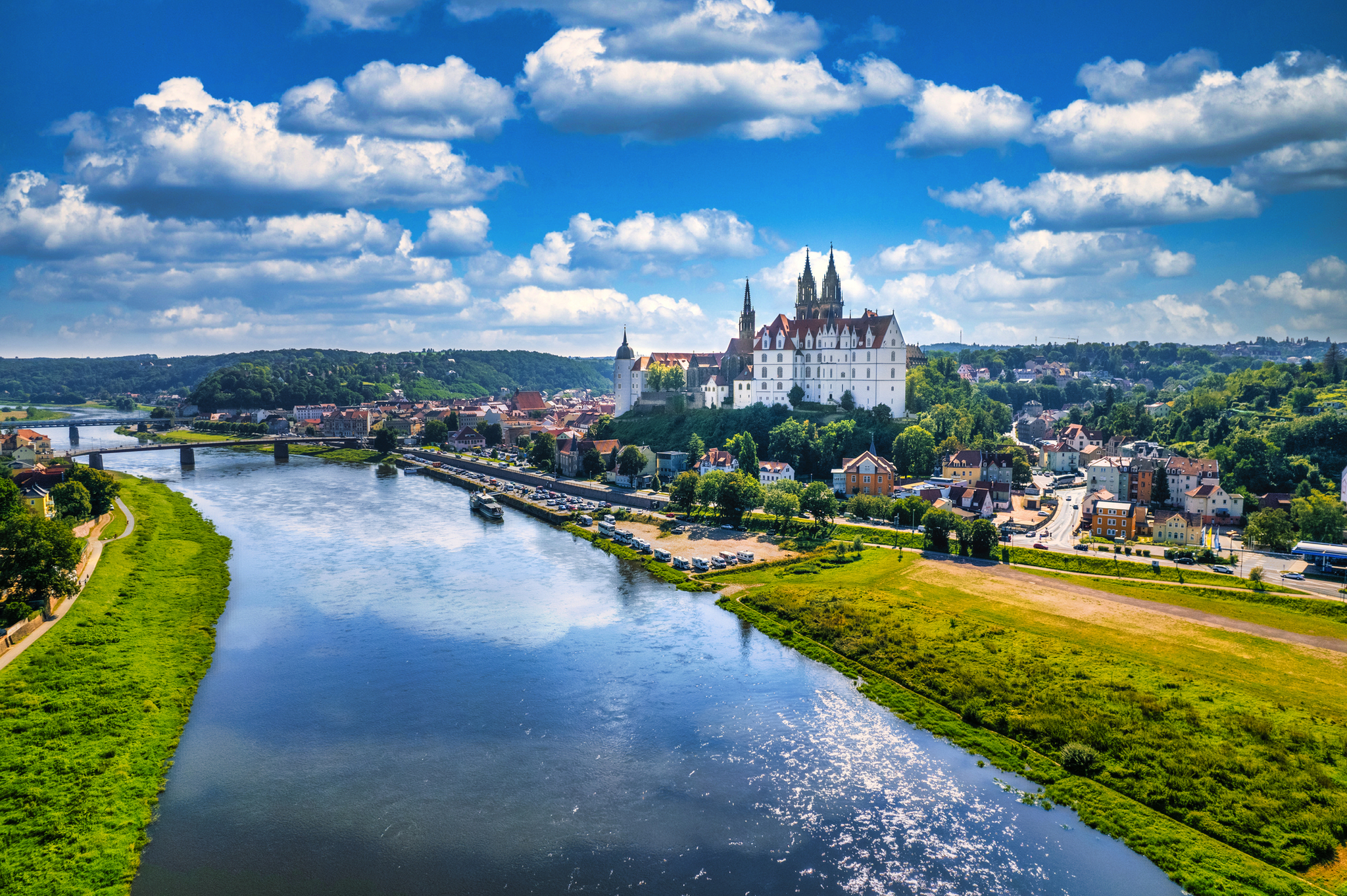 Landschaft mit Fluss, Brücke und Schloss unter blauem Himmel.