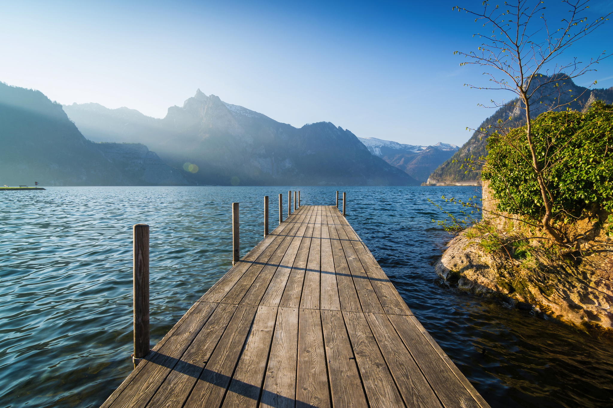 Holzsteg über ruhigen See mit Bergen im Hintergrund bei Sonnenaufgang