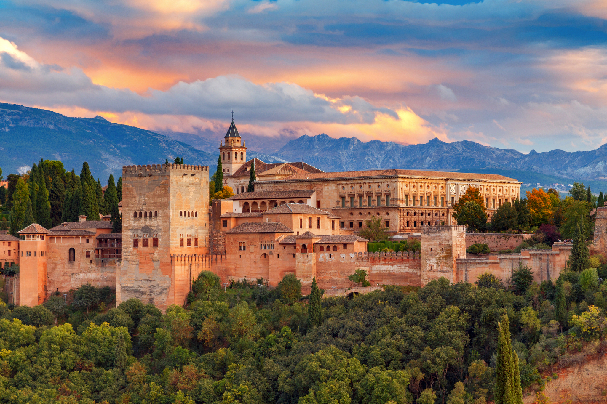 Blick auf die Alhambra in Granada bei Sonnenuntergang mit Bergen im Hintergrund.