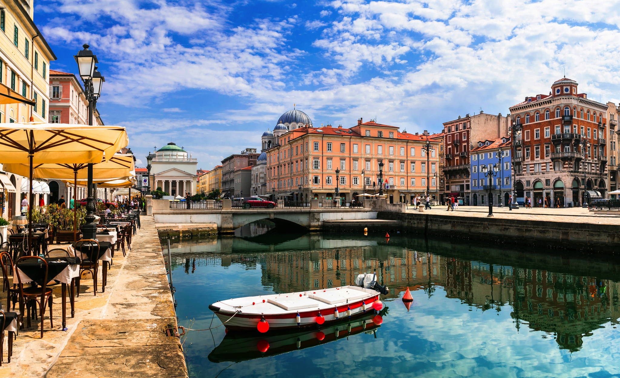 Kanal mit Boot, umgeben von historischen Gebäuden und Straßencafés unter blauem Himmel.