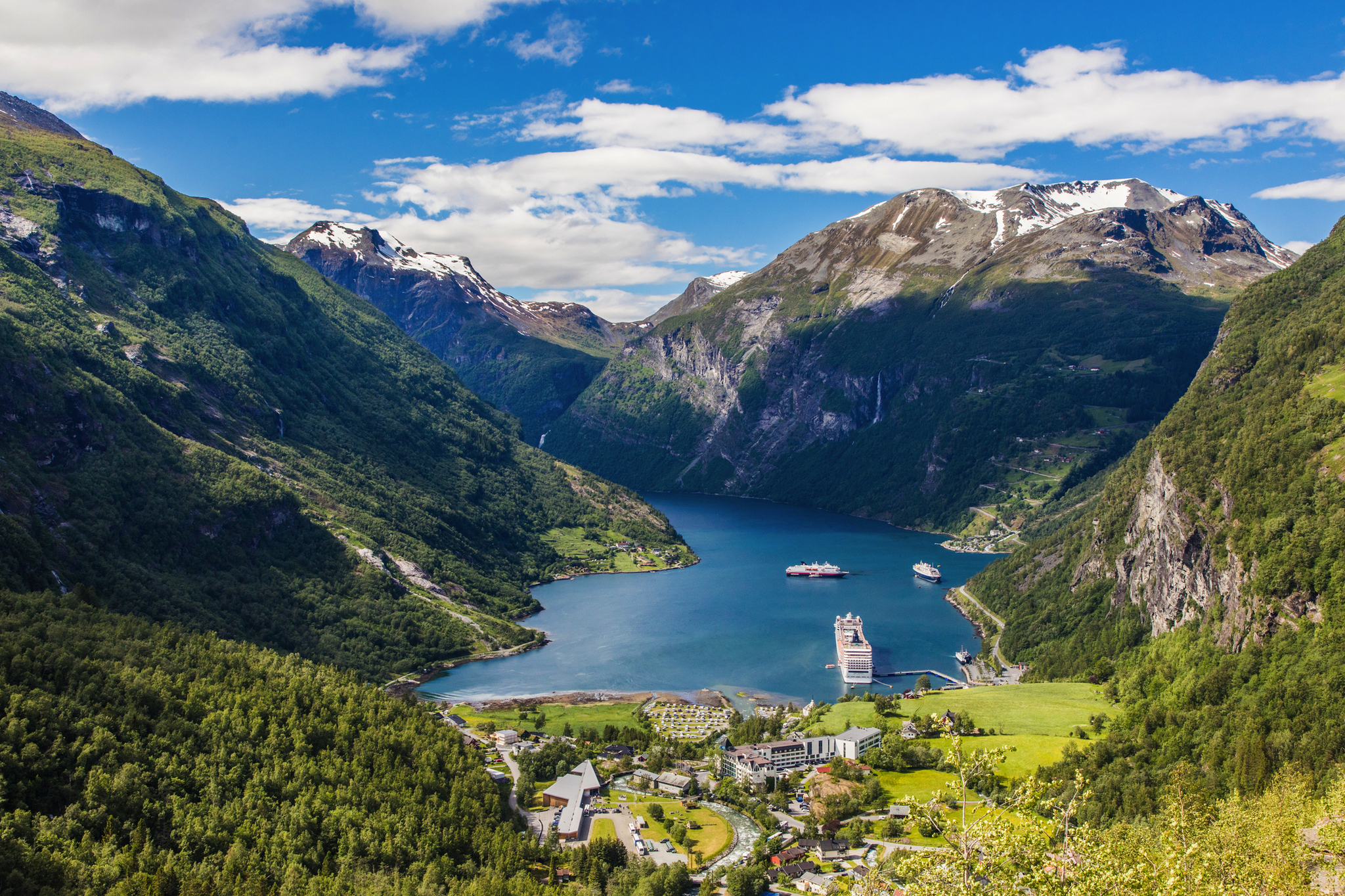 Blick auf den Geirangerfjord mit Bergen und einem Kreuzfahrtschiff im Wasser.