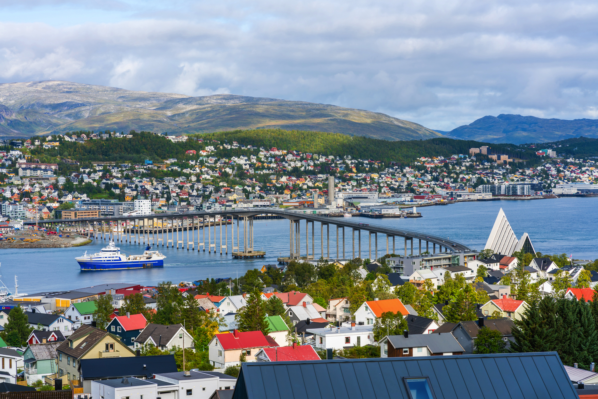 Küstenstadt mit Brücke, Schiff und Bergen im Hintergrund.