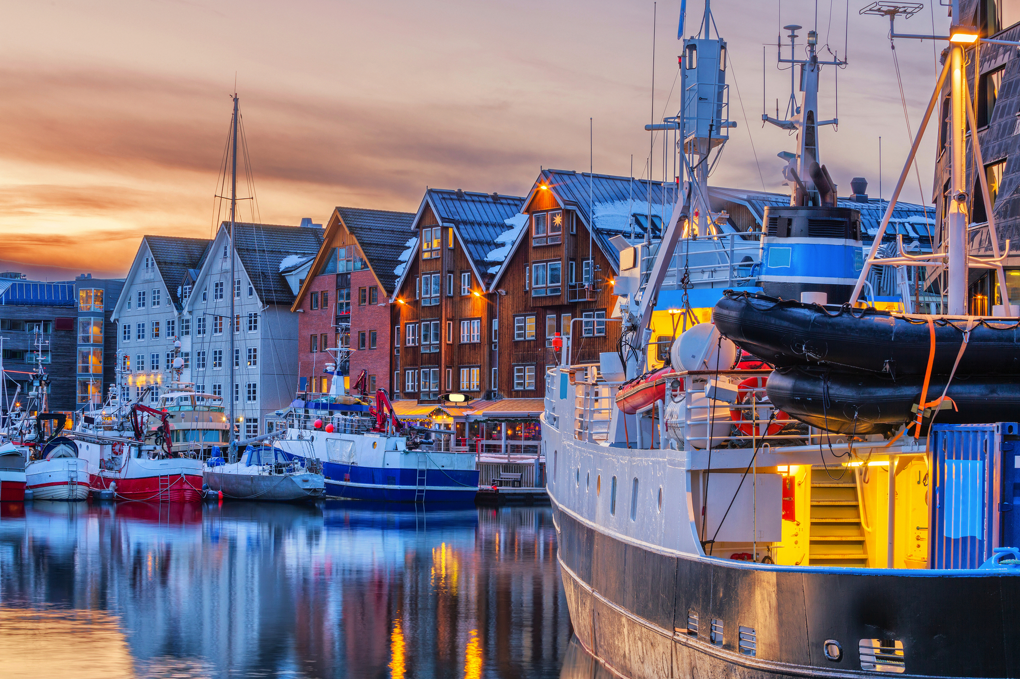 Hafen von Tromsø im Winter mit bunten Häusern und Schiffen im Wasser bei Sonnenuntergang.