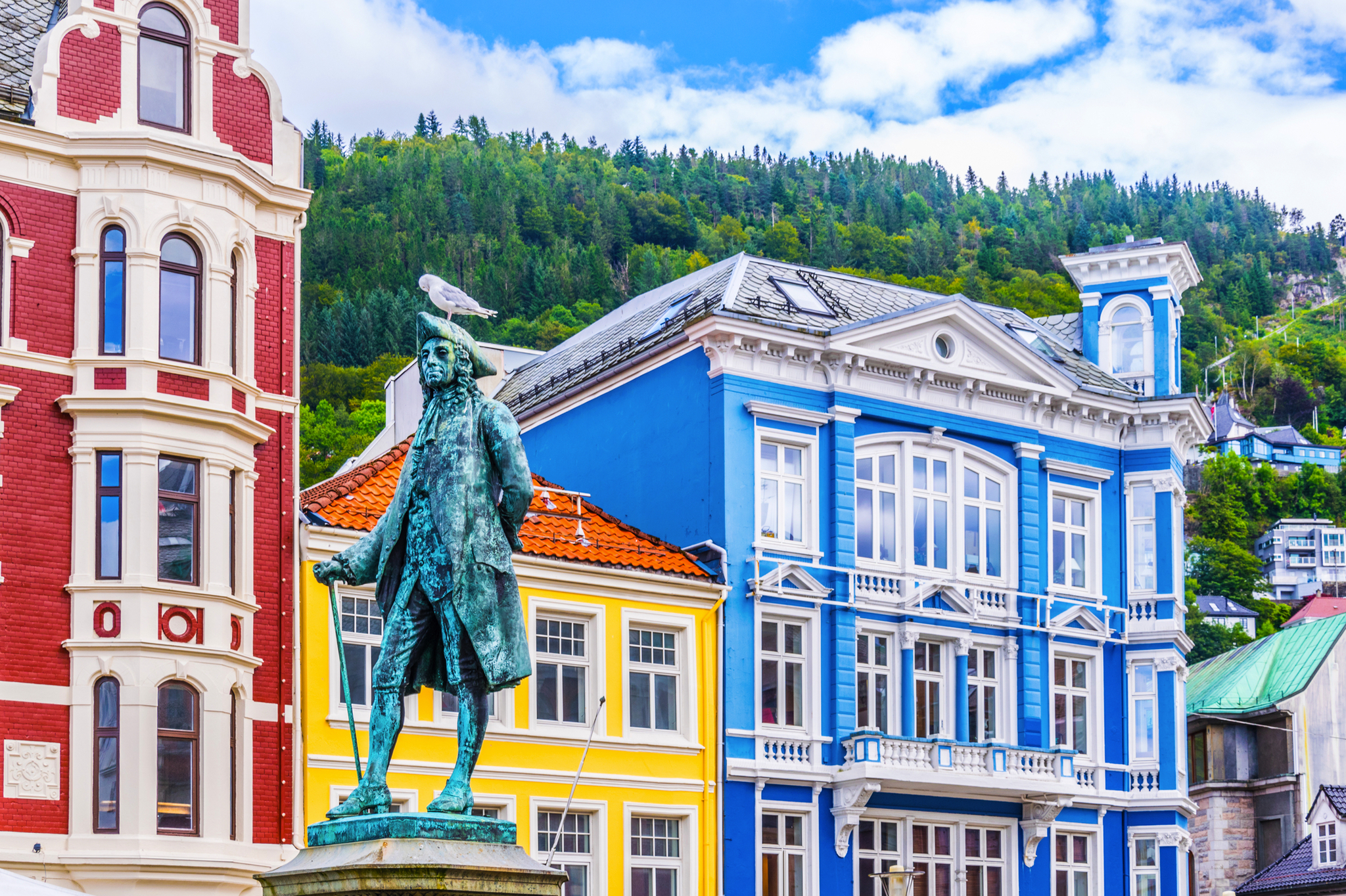 Statue mit Möwe, bunte Gebäude und bewaldeter Hügel im Hintergrund.