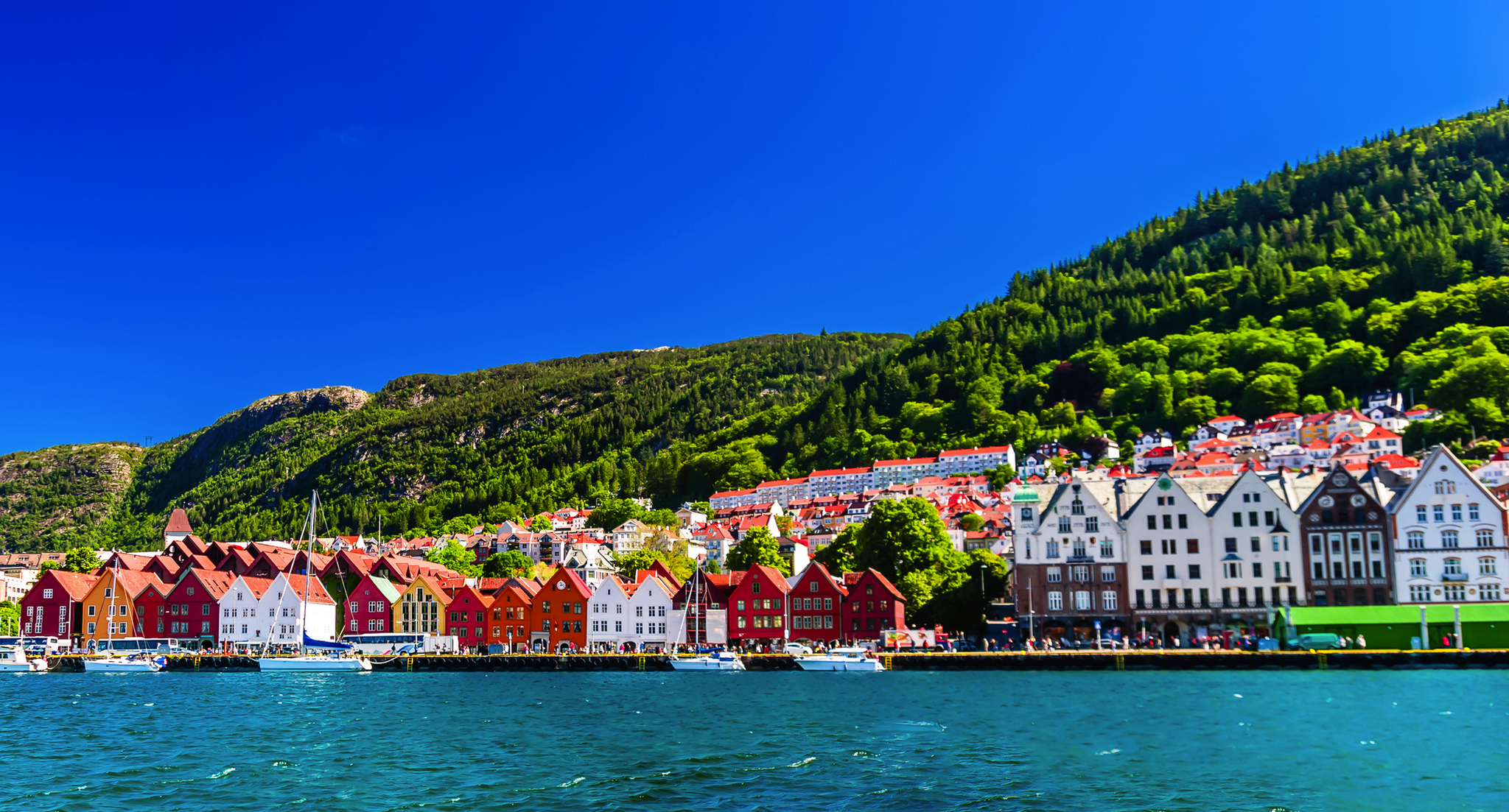 Häuserreihe am Wasser mit Bergen im Hintergrund bei klarem Himmel.
