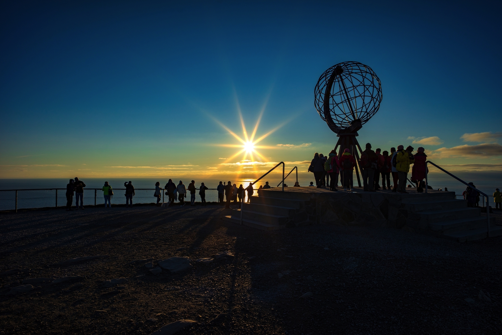 Personen bei Sonnenuntergang am Nordkap mit Globus-Skulptur.