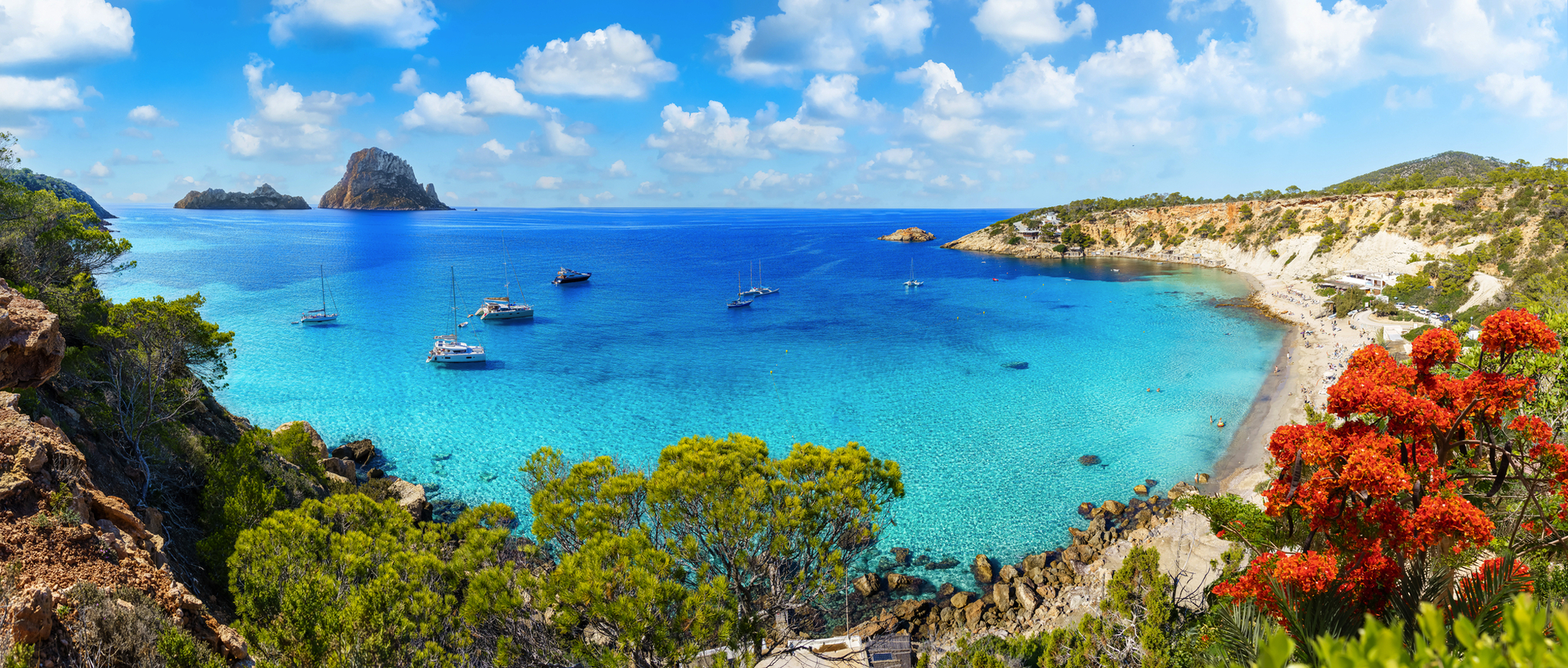 Luftaufnahme von Cala d'Hort auf Ibiza mit Sandstrand und der Felseninsel Es Vedrà im Hintergrund.
