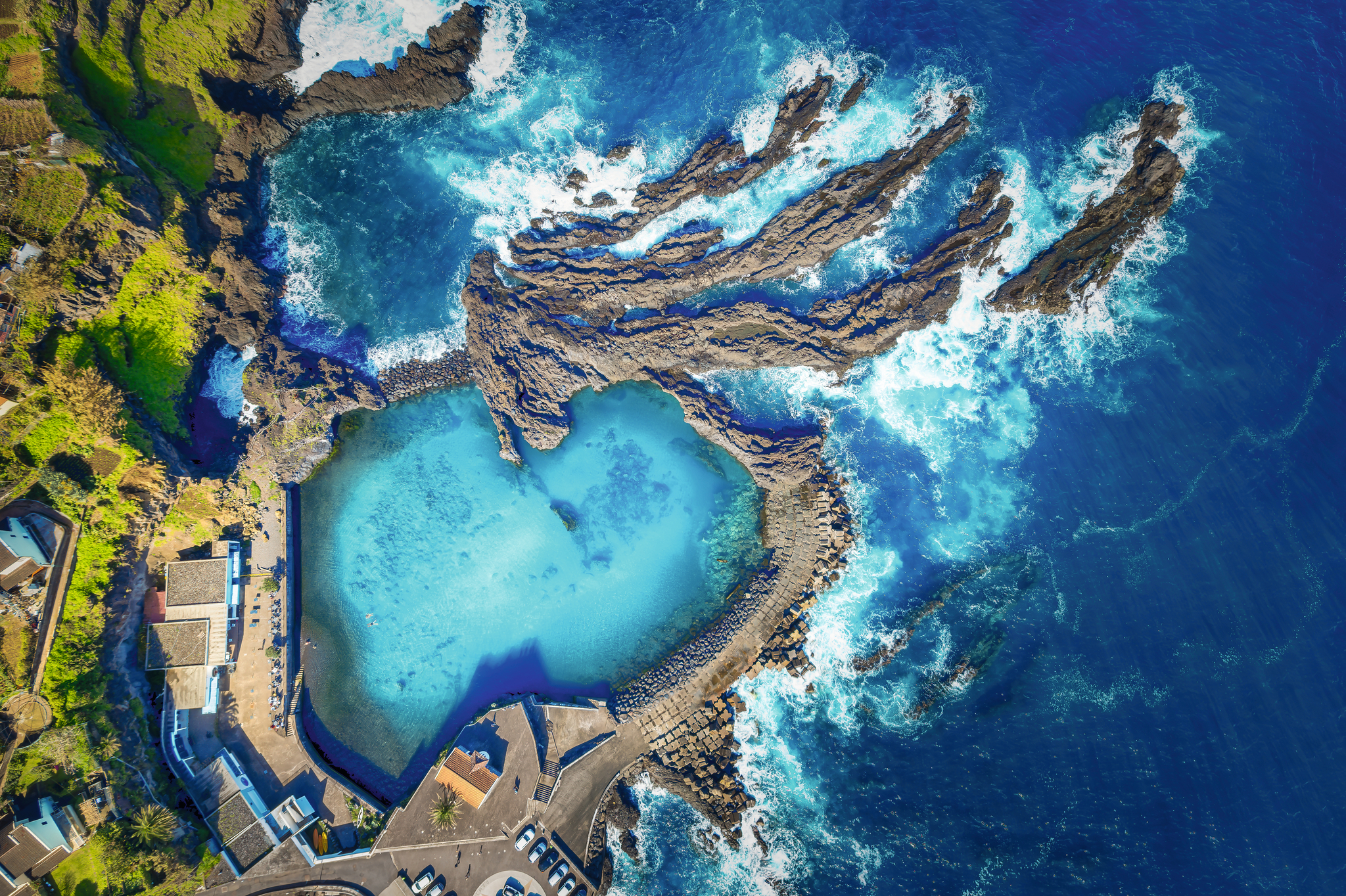 Luftaufnahme eines natürlichen Pools an einer felsigen Küste mit blauem Wasser.