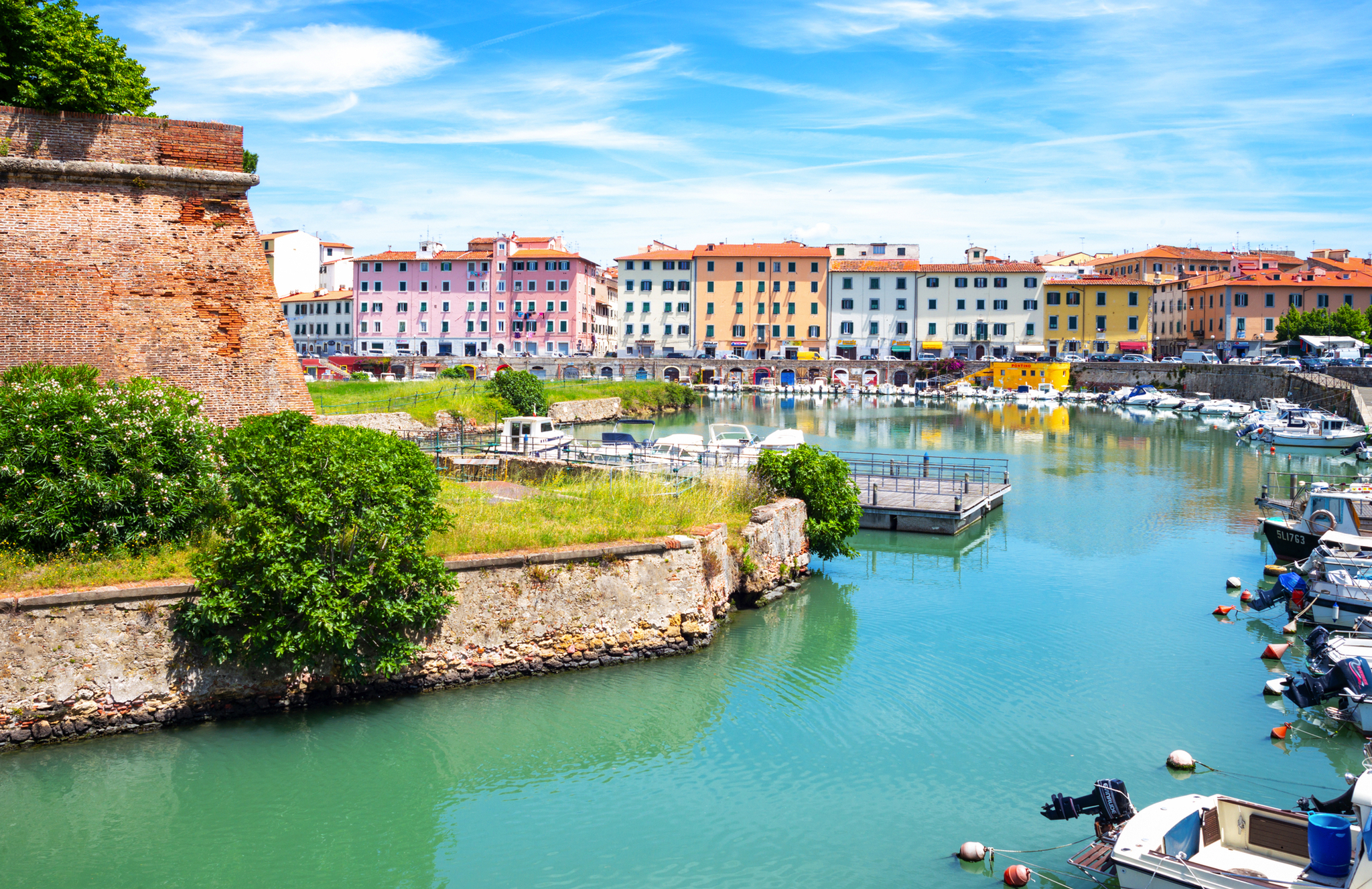 Bunte Gebäude am Wasser mit Booten und einer historischen Mauer bei klarem Himmel.