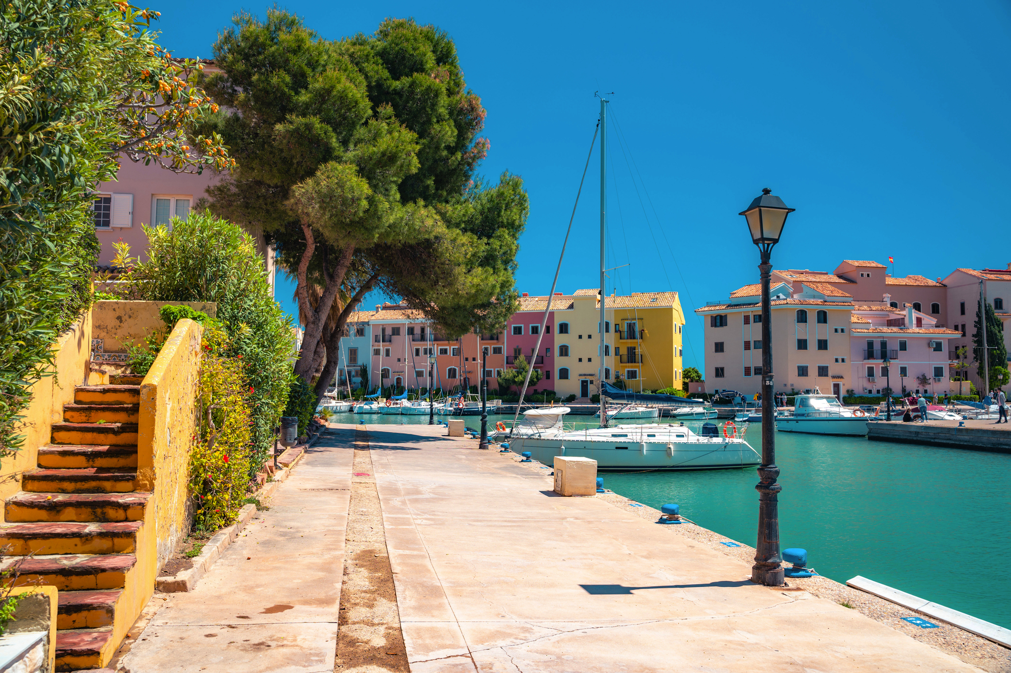 Promenade mit Booten im Yachthafen, umgeben von farbigen Gebäuden und Bäumen.