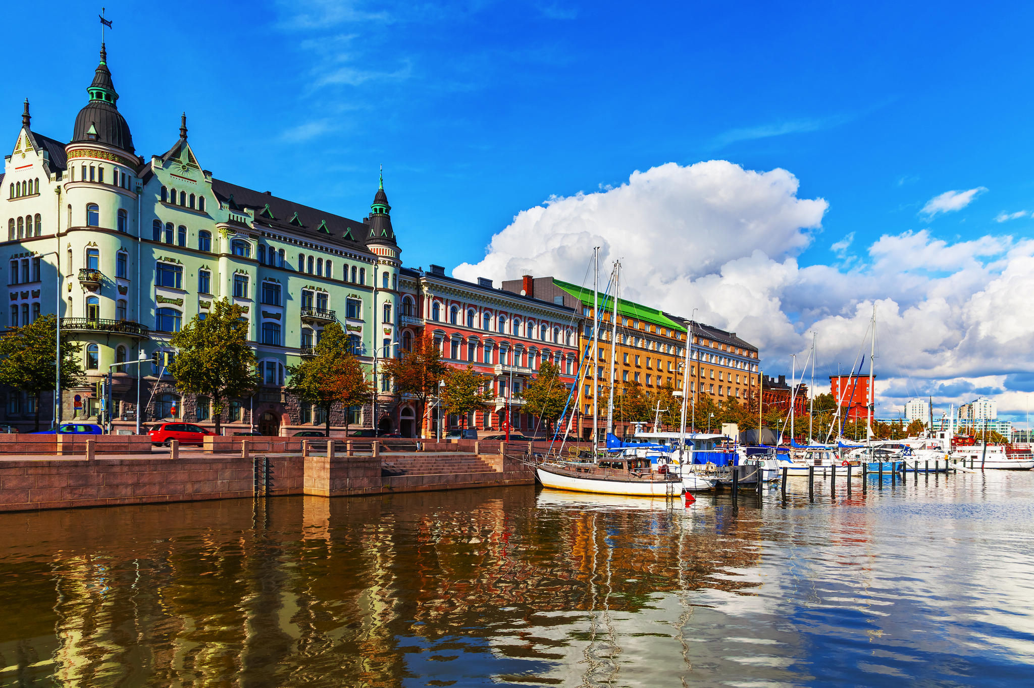 Altstadtpier in Helsinki mit historischen Gebäuden und Segelbooten vor blauem Himmel.