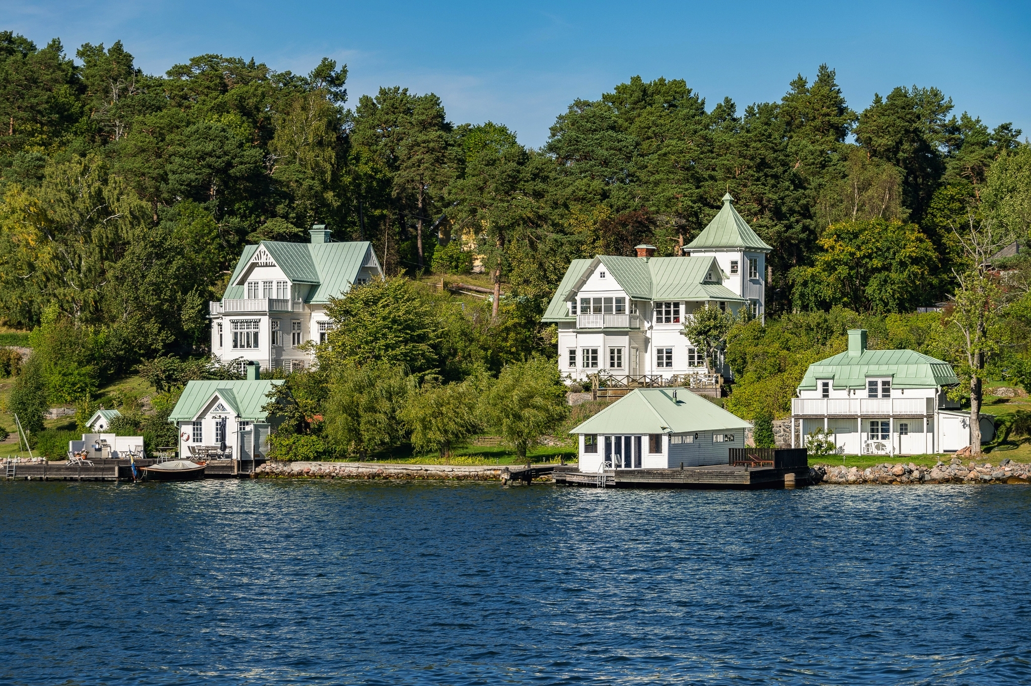 Weiße Häuser mit grünen Dächern am Wasser, eingebettet in üppige Vegetation.