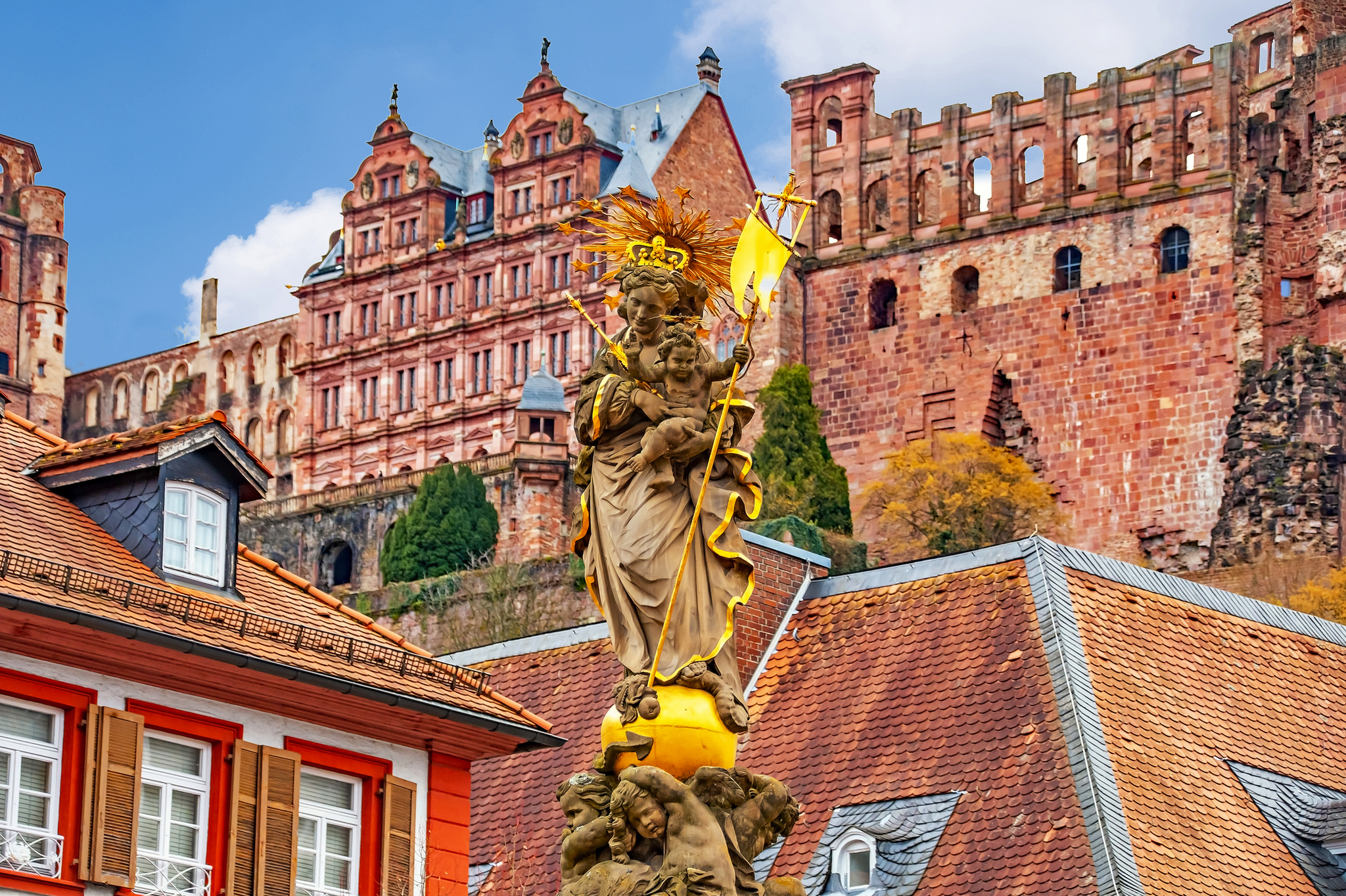 Historisches Schloss vor Wohngebäuden, mit denkmalgeschützter Statue im Vordergrund.