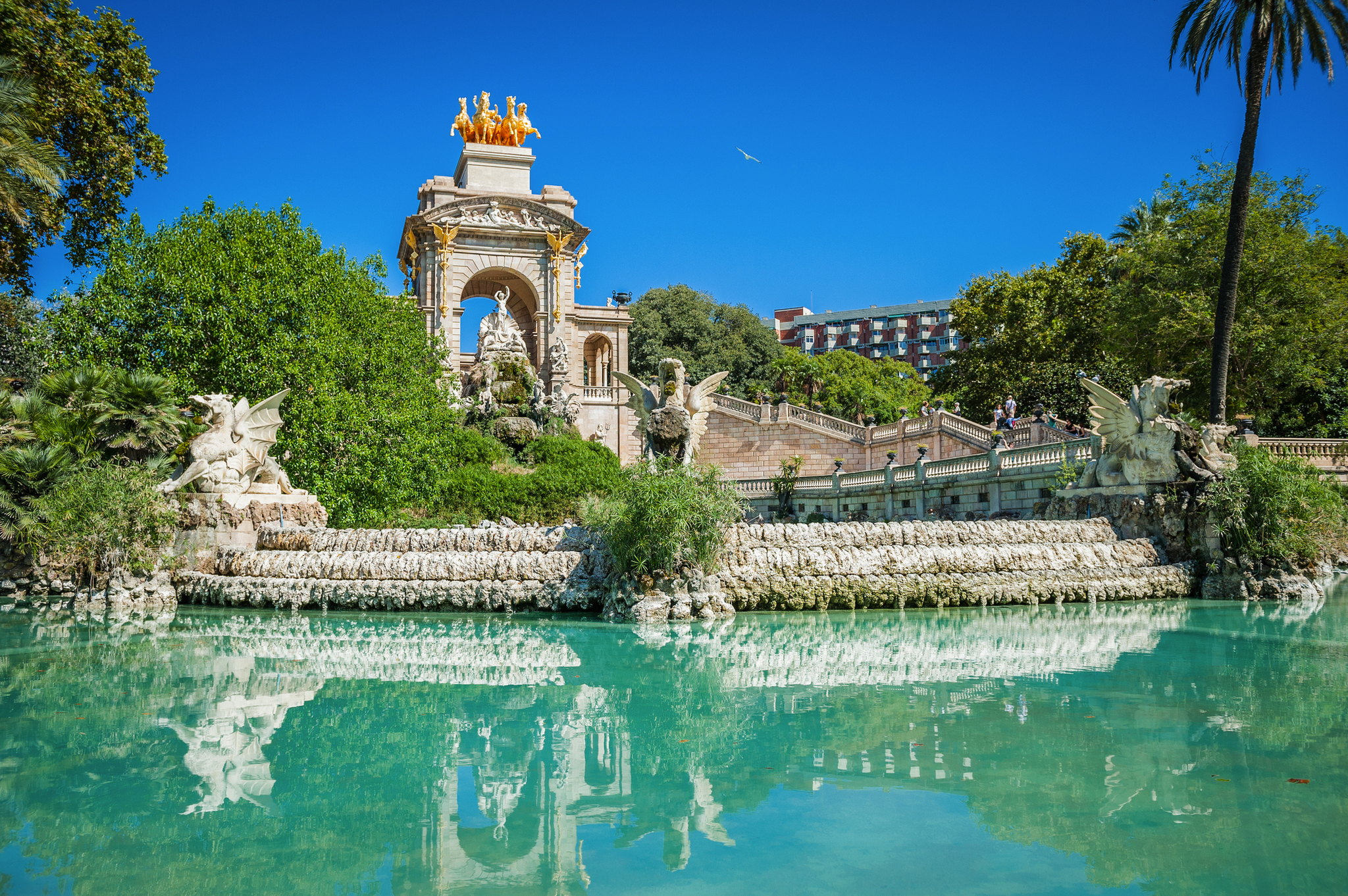 Springbrunnen und Statue in einem Park vor blauem Himmel und Palmen.