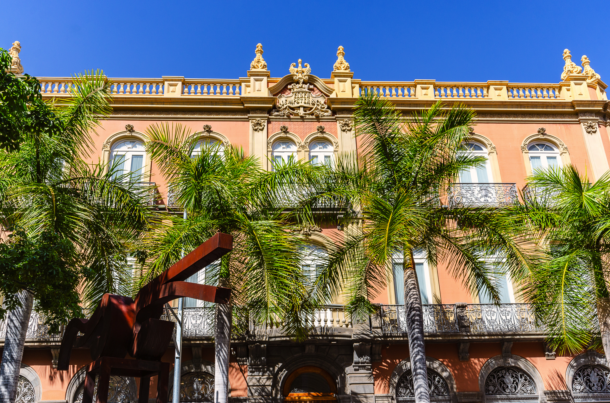 Historisches Gebäude mit Palmen im Vordergrund bei klarem Himmel.