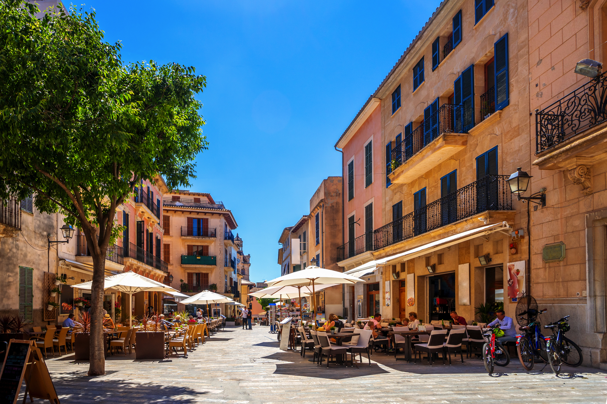 Straßencafé in einer sonnigen europäischen Altstadt mit Menschen und Fahrrädern.