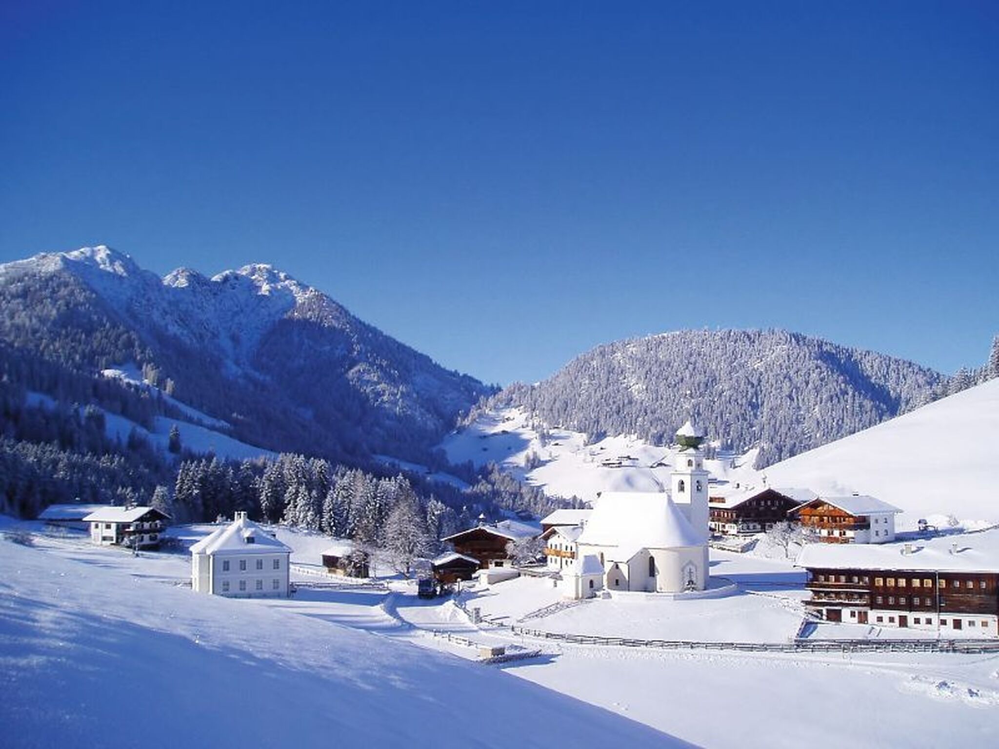 Winterliche Dorflandschaft in Thierbach, Wildschönau mit verschneiten Bergen im Hintergrund.