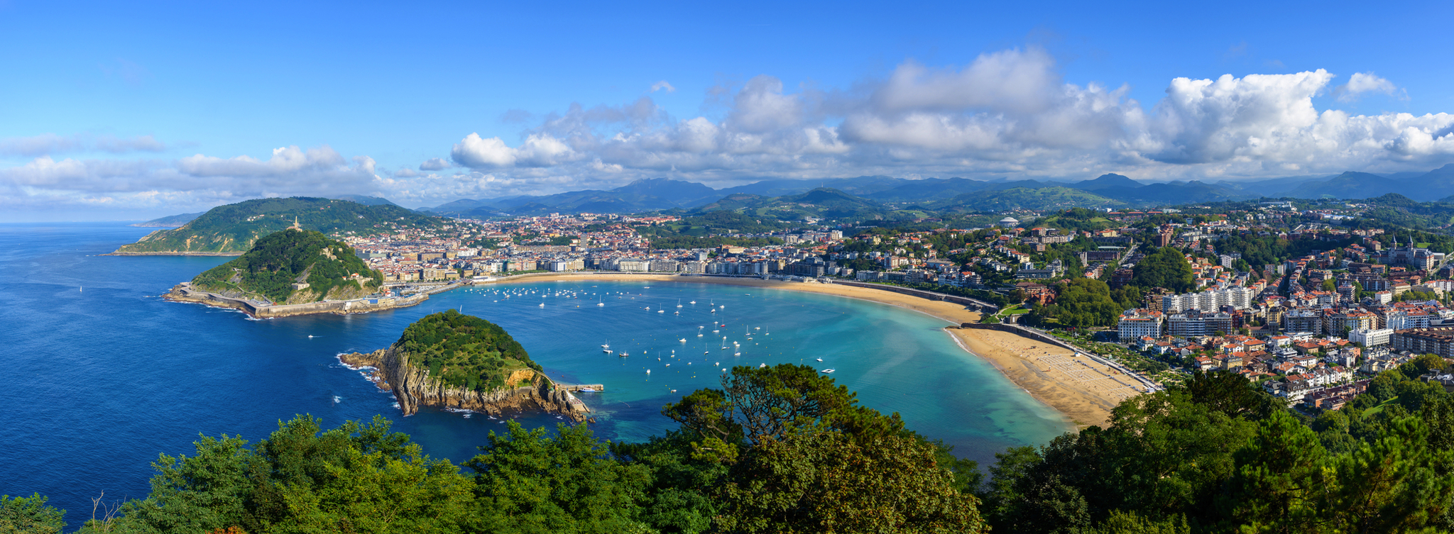 Panoramablick auf eine Küstenstadt mit Sandstrand und Hafen bei klarem Himmel.