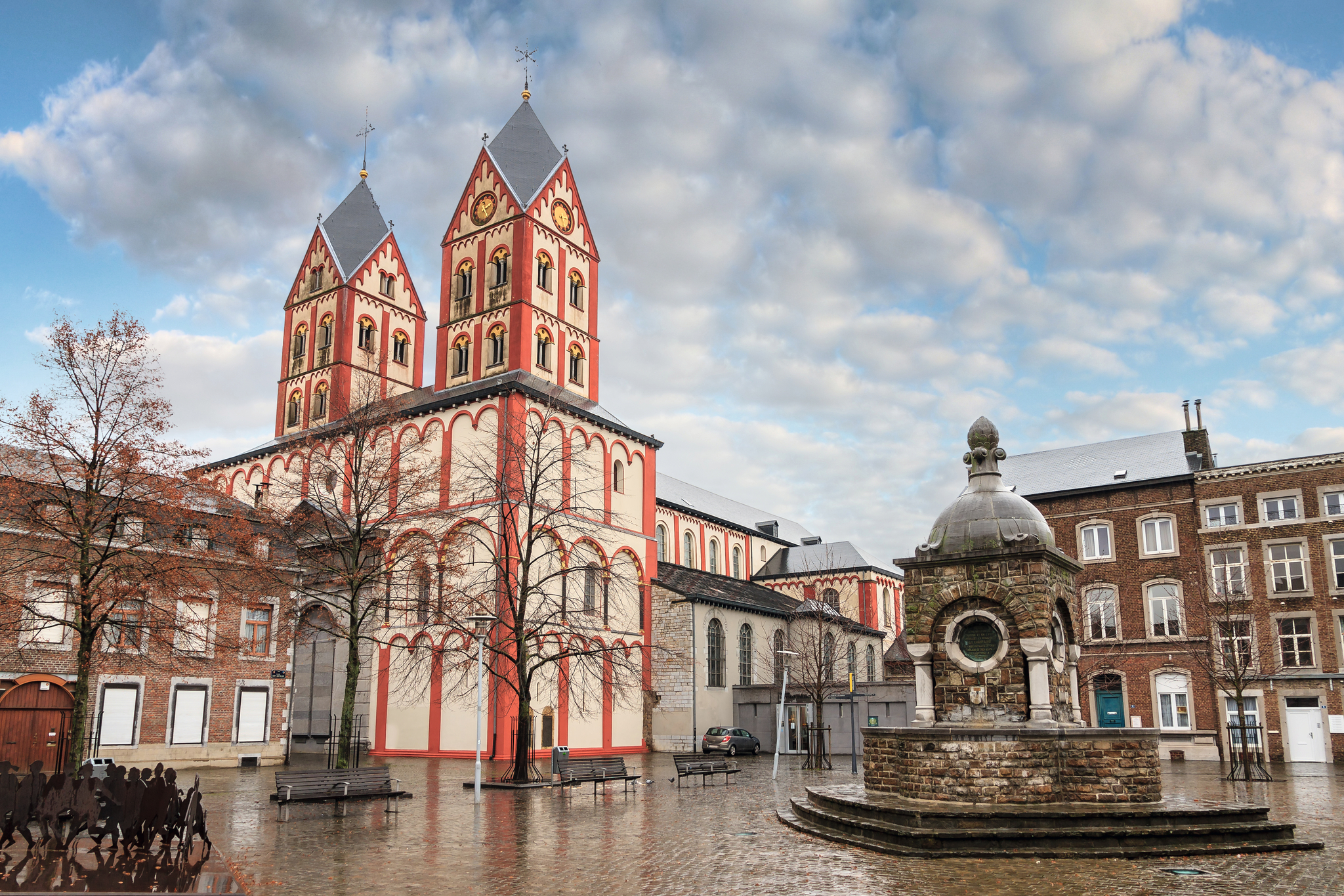 Kirche mit zwei Türmen und Brunnen auf einem Platz bei bewölktem Himmel.