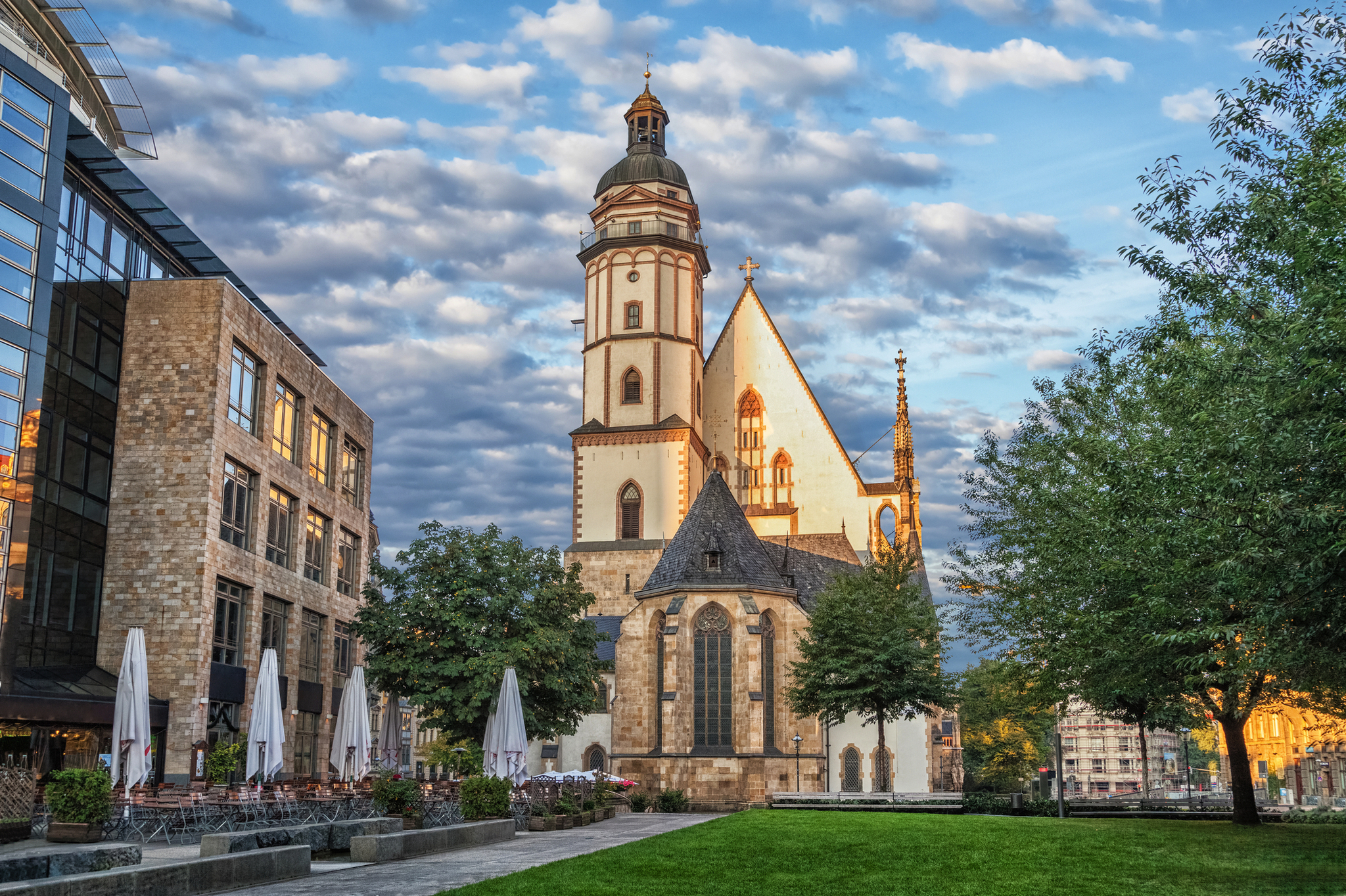 Kirche mit imposantem Turm neben modernen Gebäuden unter bewölktem Himmel.