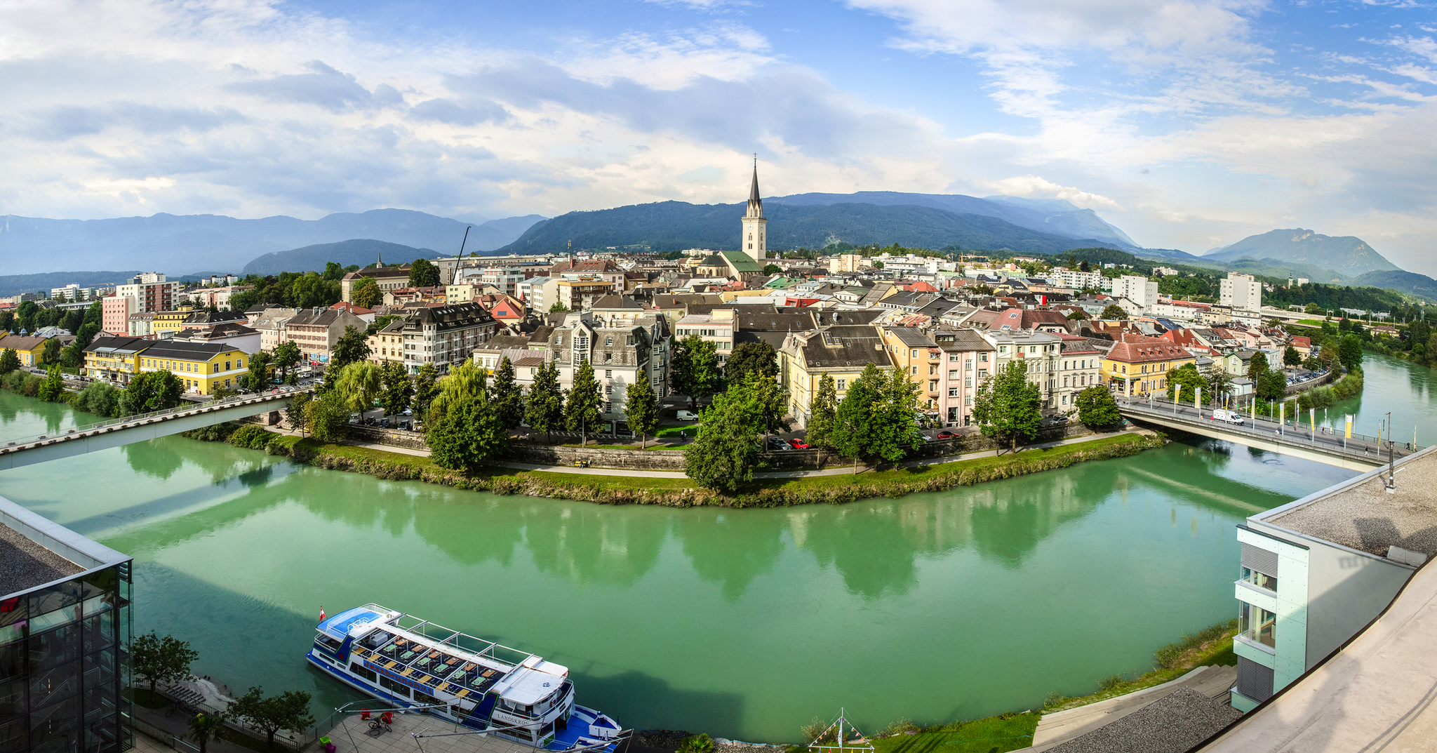 Stadtansicht mit Fluss, Kirche und Boot im Vordergrund.
