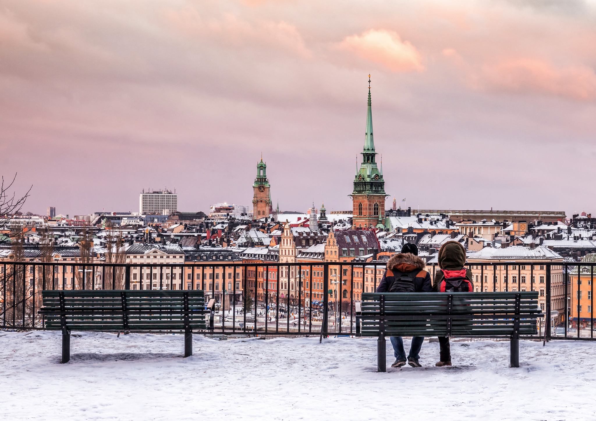 Pärchen sitzt auf Bank, mit Blick auf verschneite Stadt und Kirchtürme.