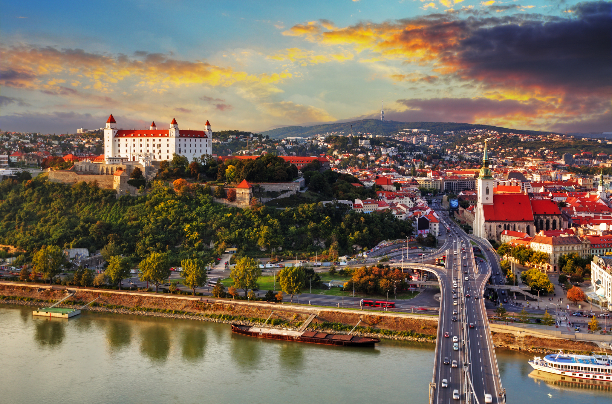 Stadtansicht von Bratislava mit Burg und Fluss bei Sonnenuntergang.