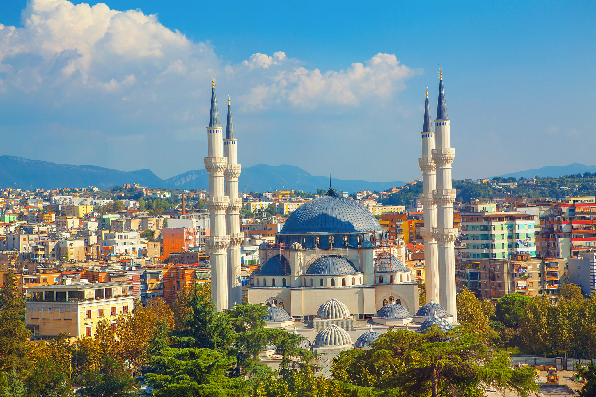 Große Moschee mit vier Minaretten vor Stadt- und Berghintergrund.