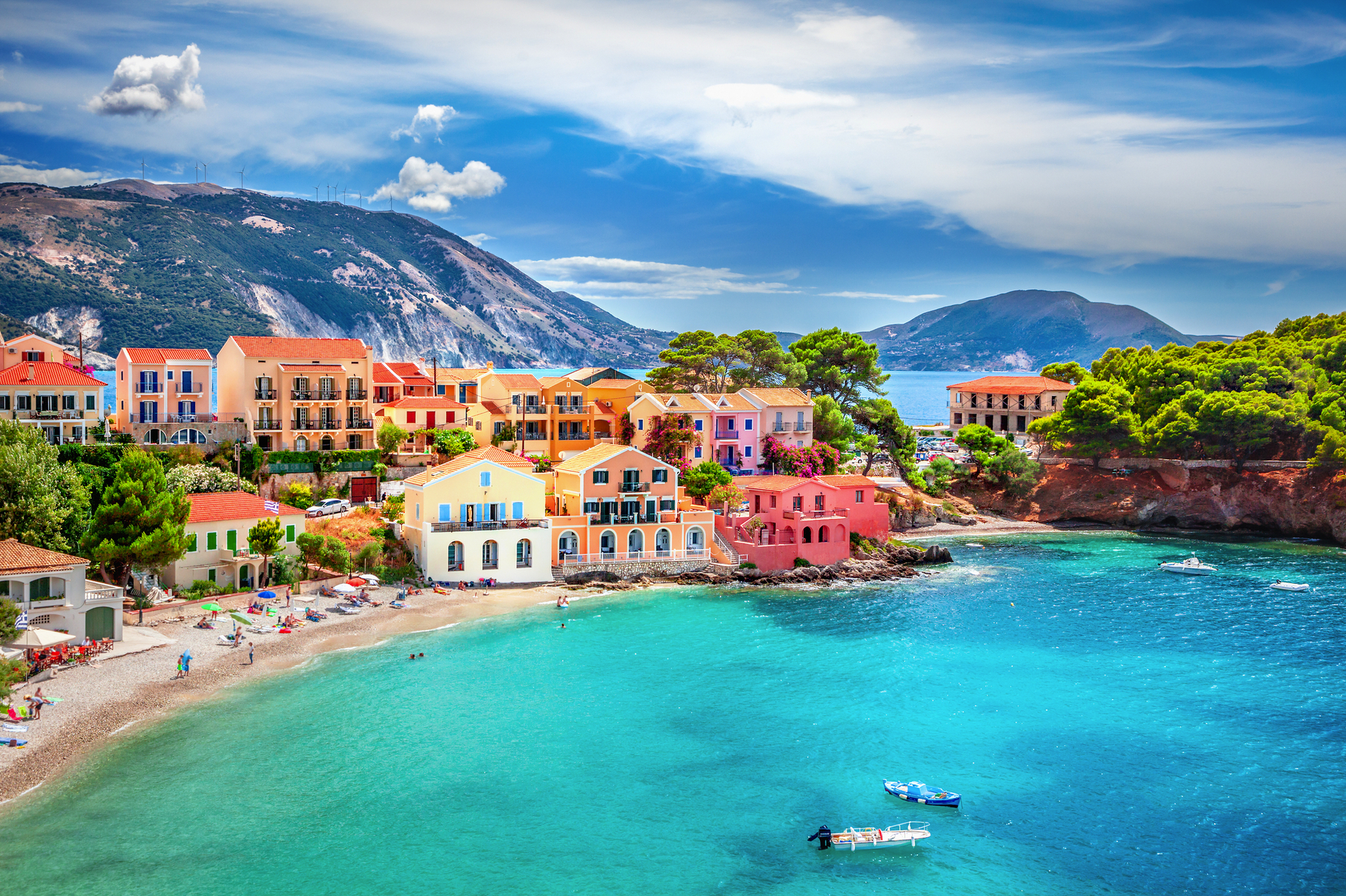 Bunte Häuser am Meer mit klarem, blauem Wasser und grünen Hügeln im Hintergrund.