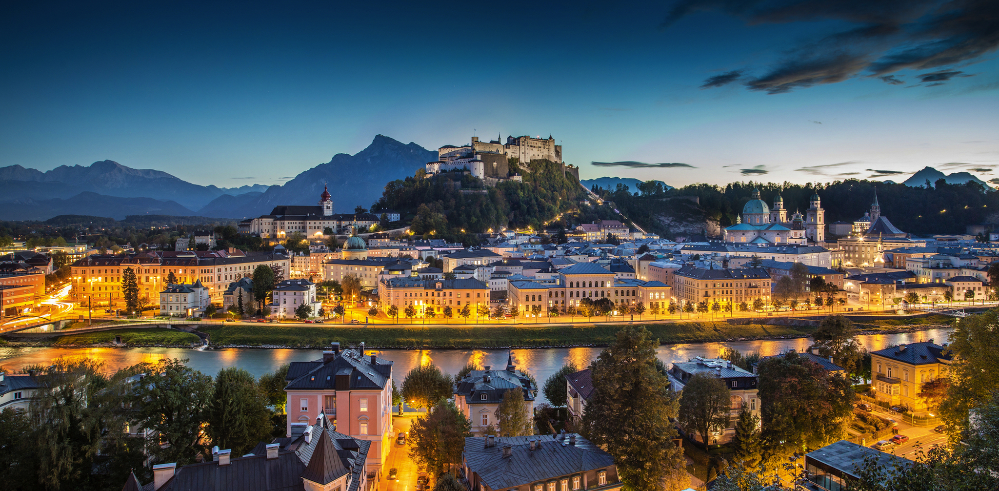 Stadtansicht von Salzburg bei Dämmerung mit Festung Hohensalzburg im Hintergrund.