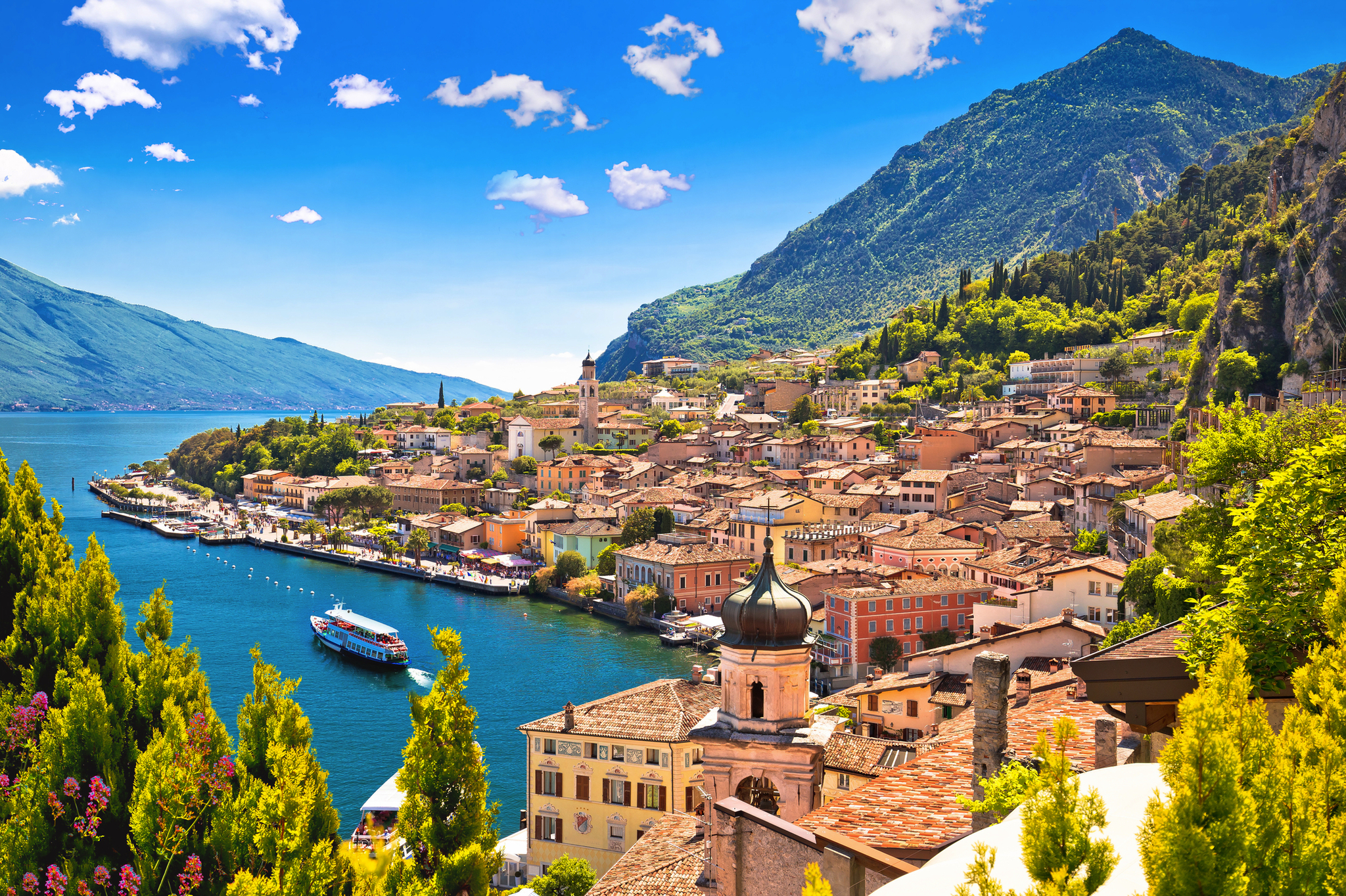 Küstenstadt am See mit Bergen im Hintergrund unter blauem Himmel.