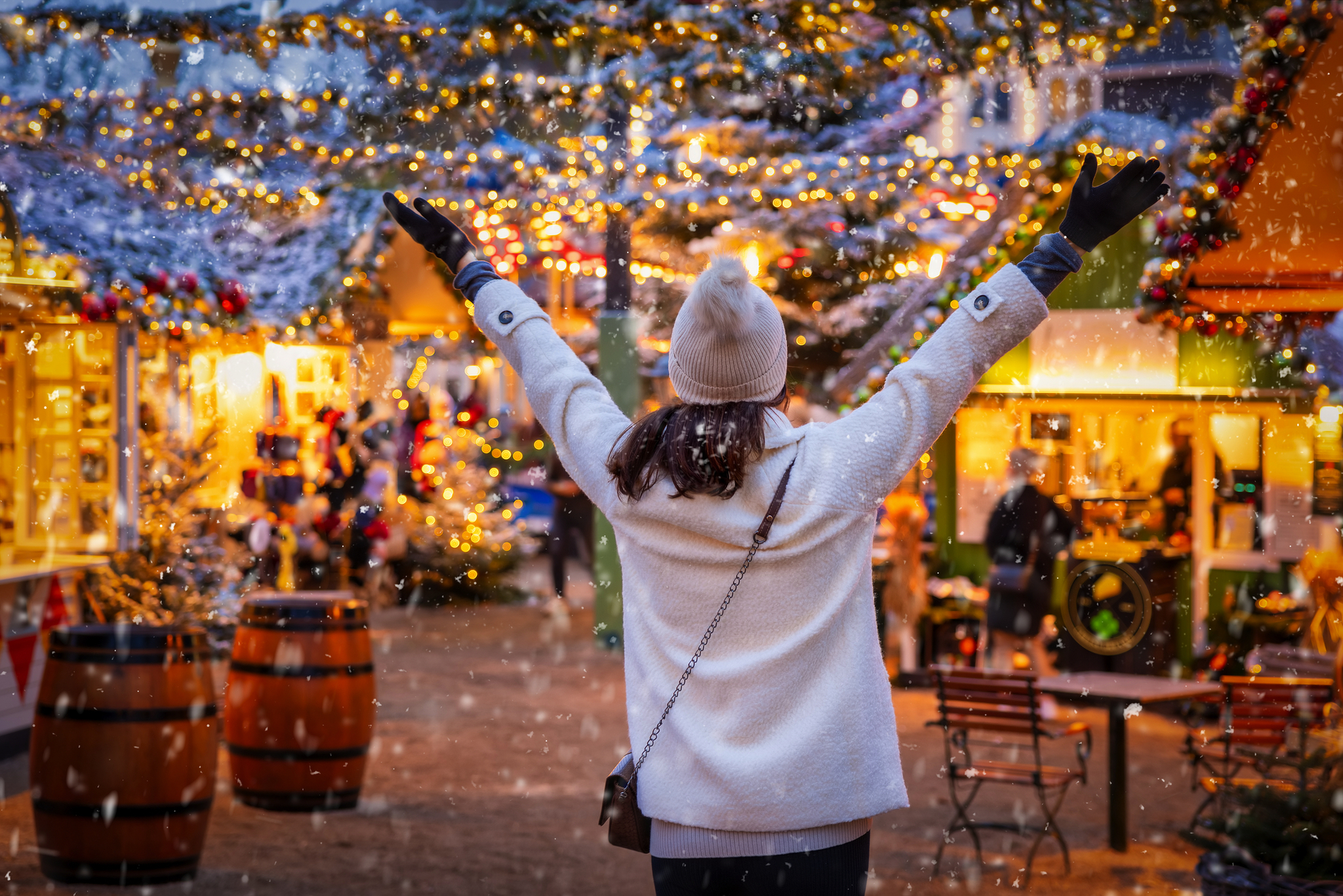 Person auf Weihnachtsmarkt, Hände hoch, umgeben von Lichtern und Dekorationen.
