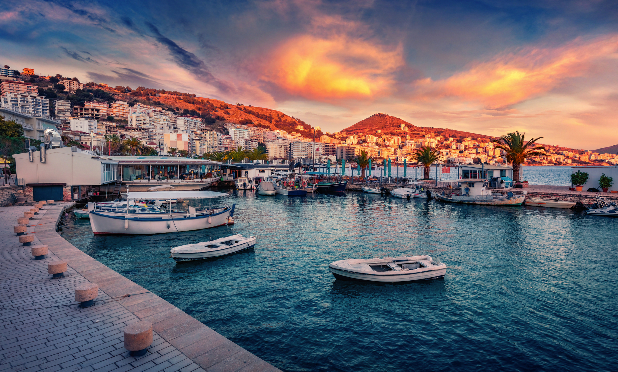 Saranda Marina bei Sonnenuntergang mit Booten und Stadtansicht im Hintergrund.