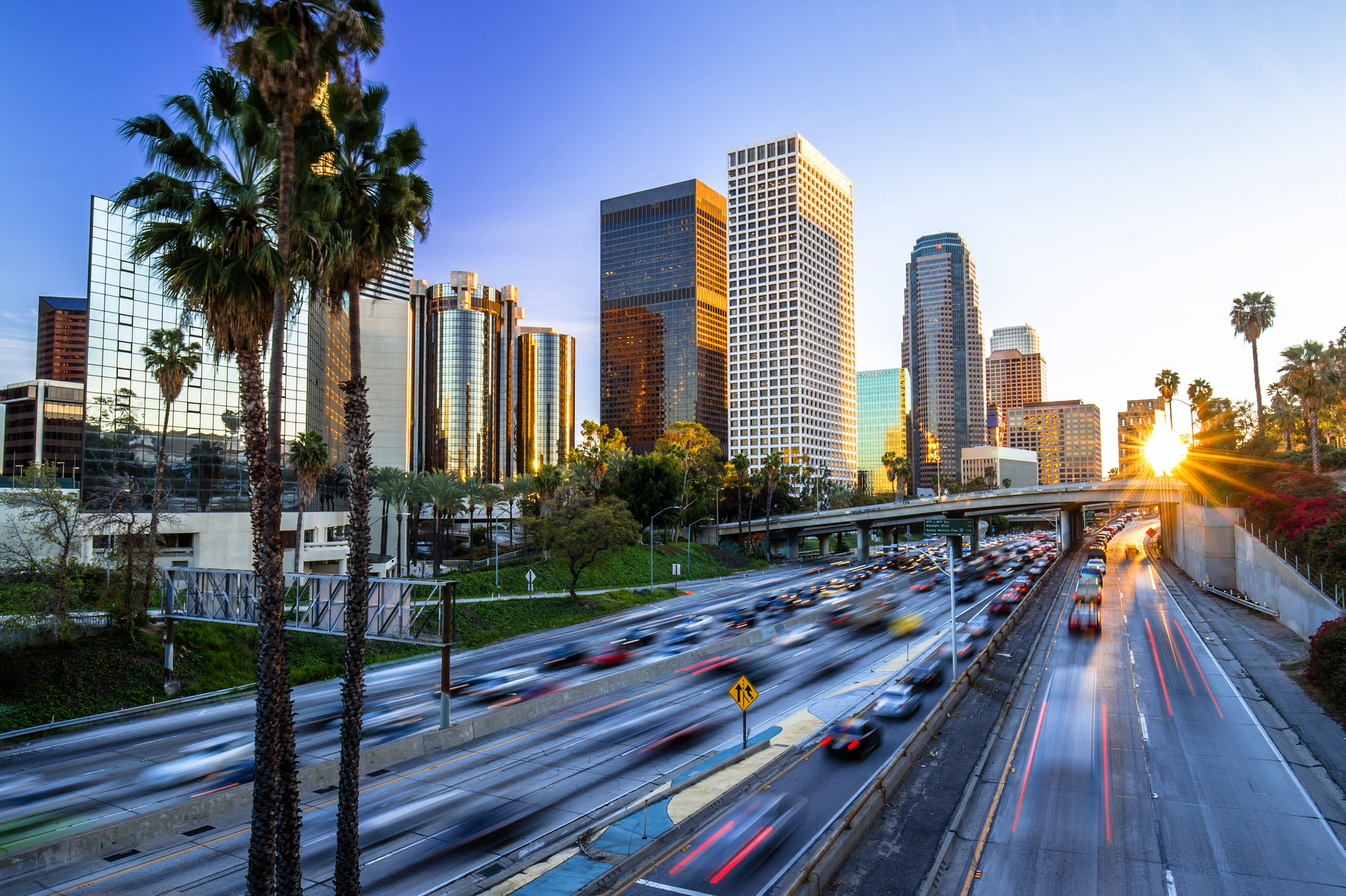Stadtansicht mit Hochhäusern, Palmen und befahrener Autobahn bei Sonnenuntergang