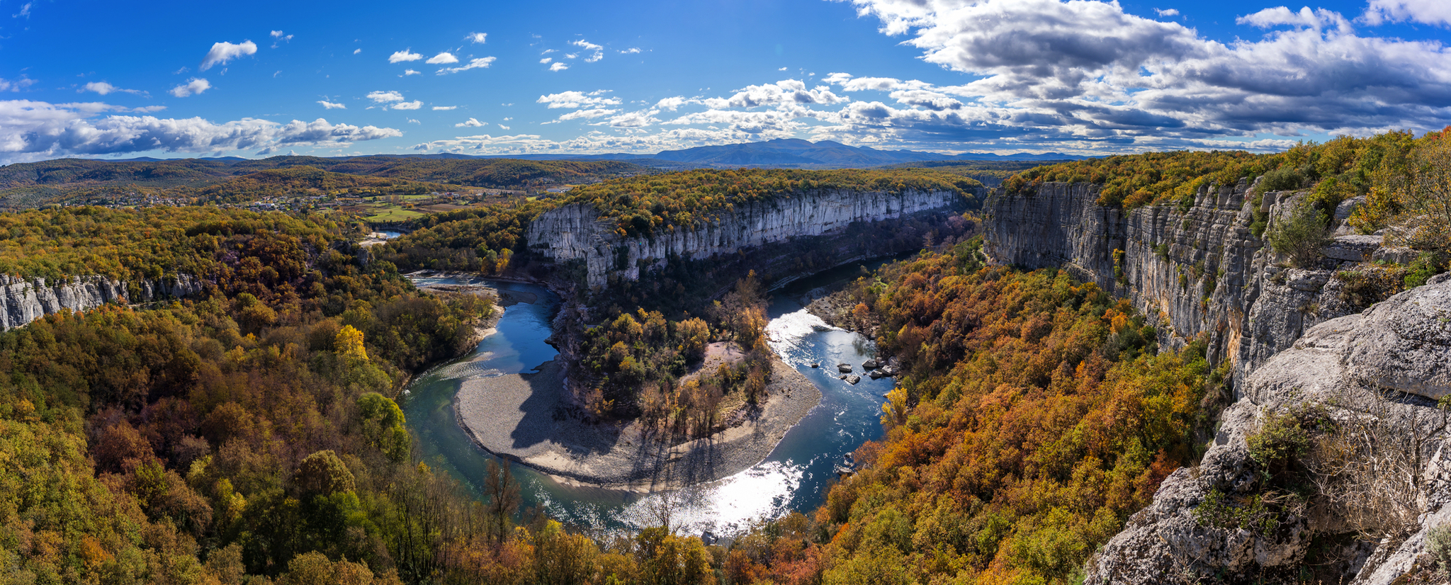 Fluss in einer Schlucht, umgeben von bewaldeten Hügeln und herbstlichem Laub.