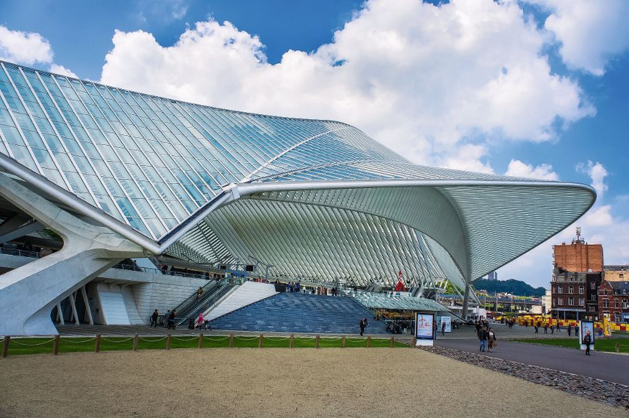Futuristischer Bahnhof mit geschwungener Glasfassade und Wolken am Himmel.