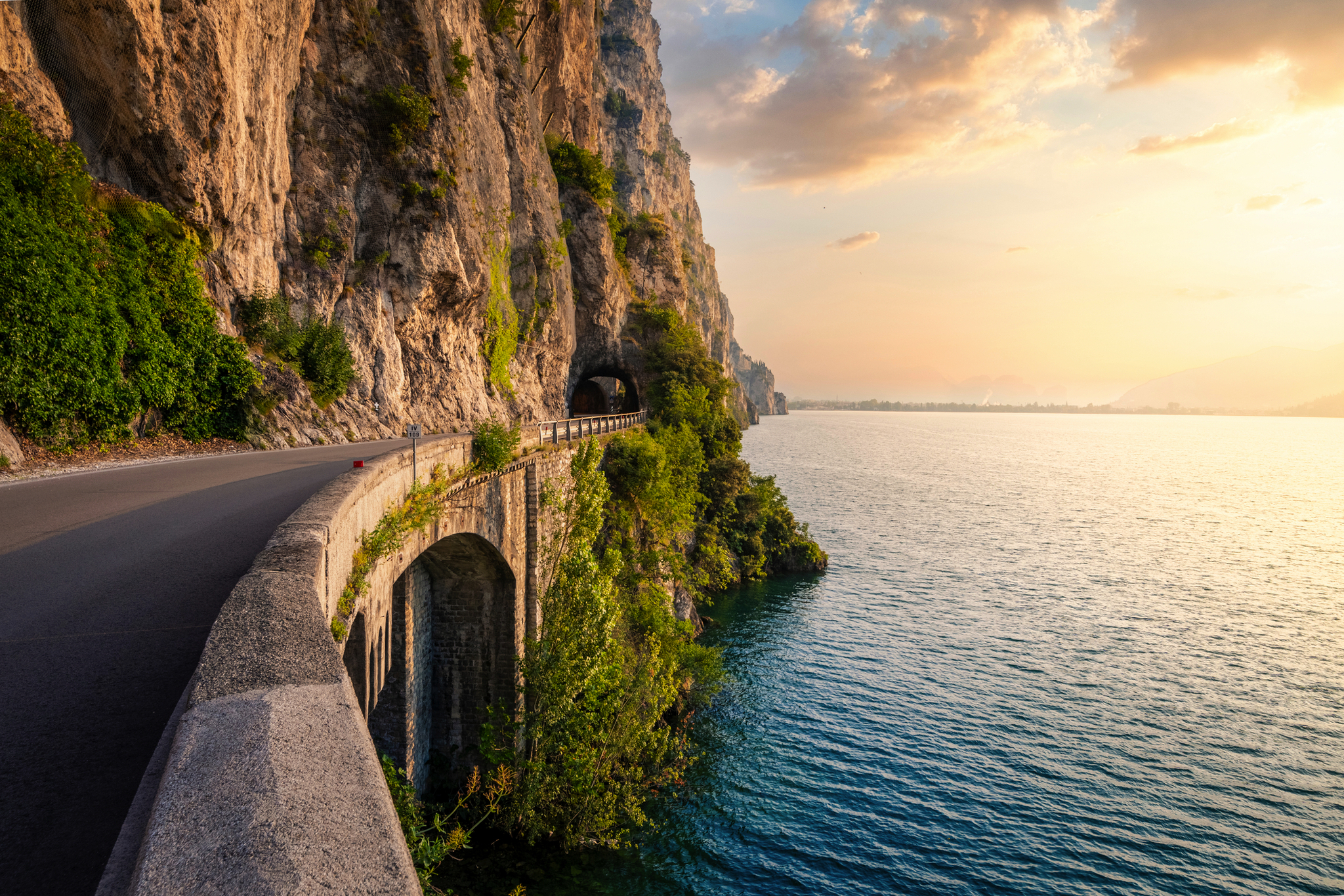 Küstenstraße entlang felsiger Klippe und See im Sonnenuntergang.