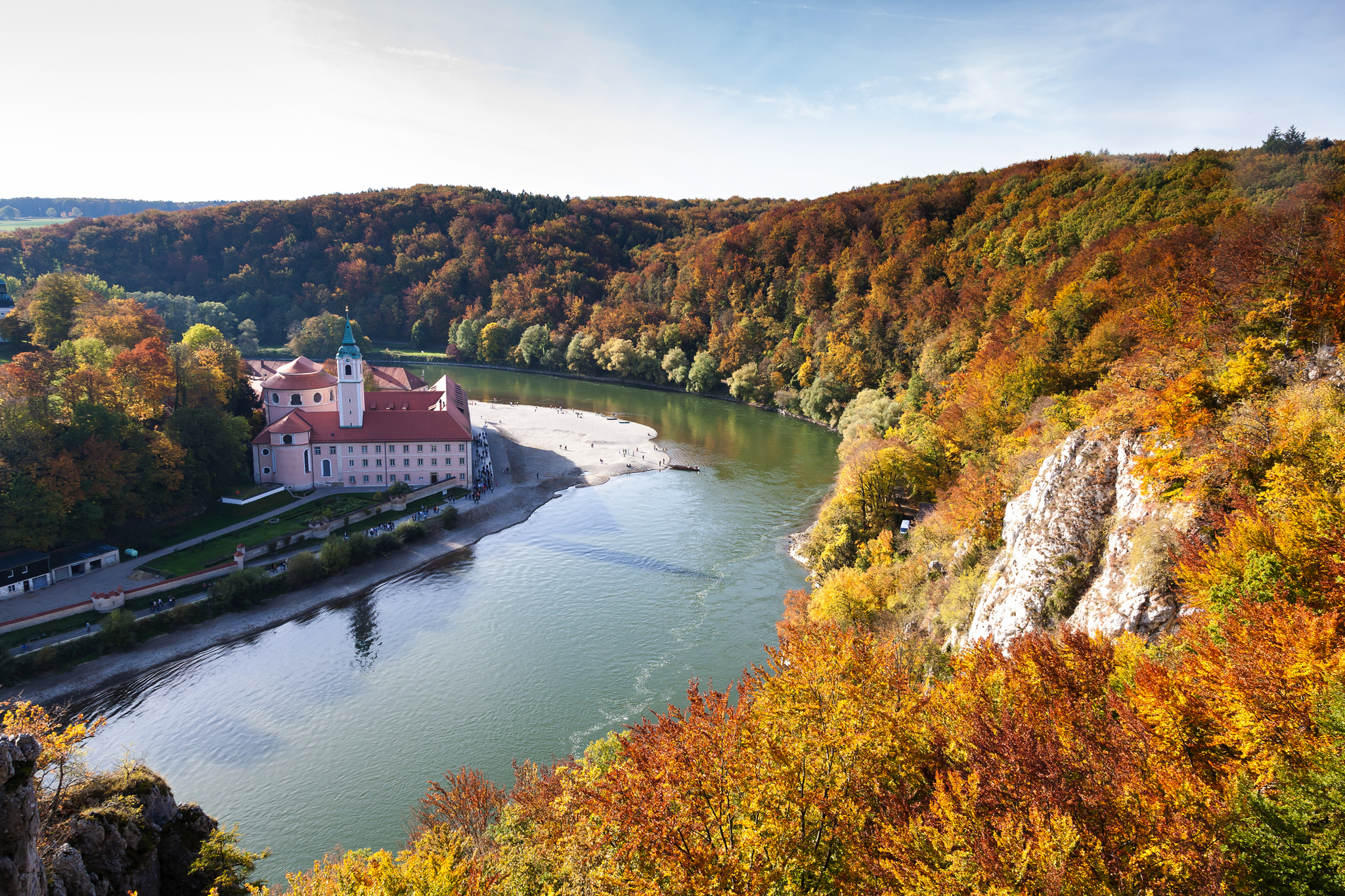 Kloster an einem Fluss in bewaldeter Hügellandschaft im Herbst.