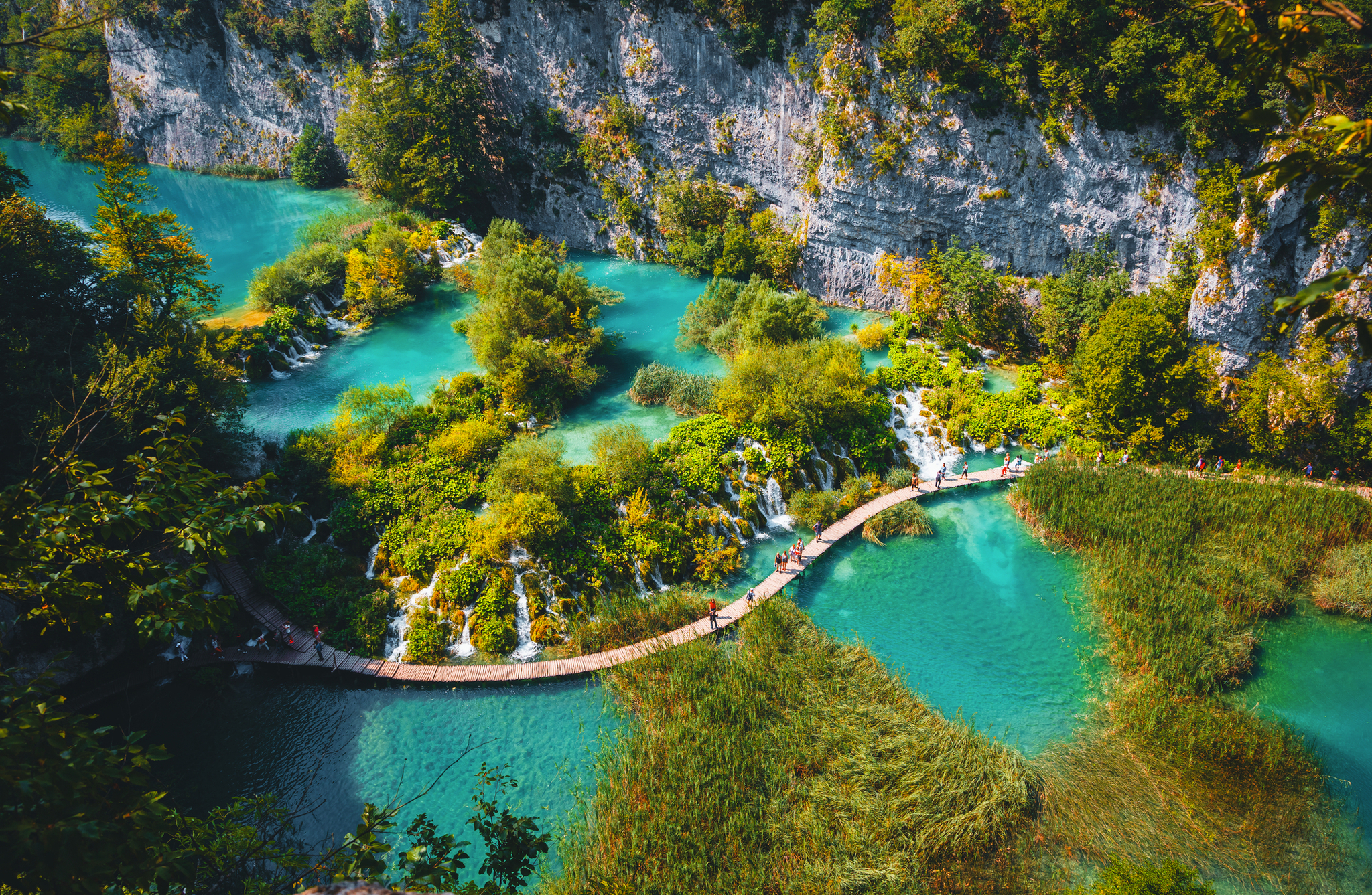 Holzsteg über türkisfarbenem See in bewaldeter Schlucht.